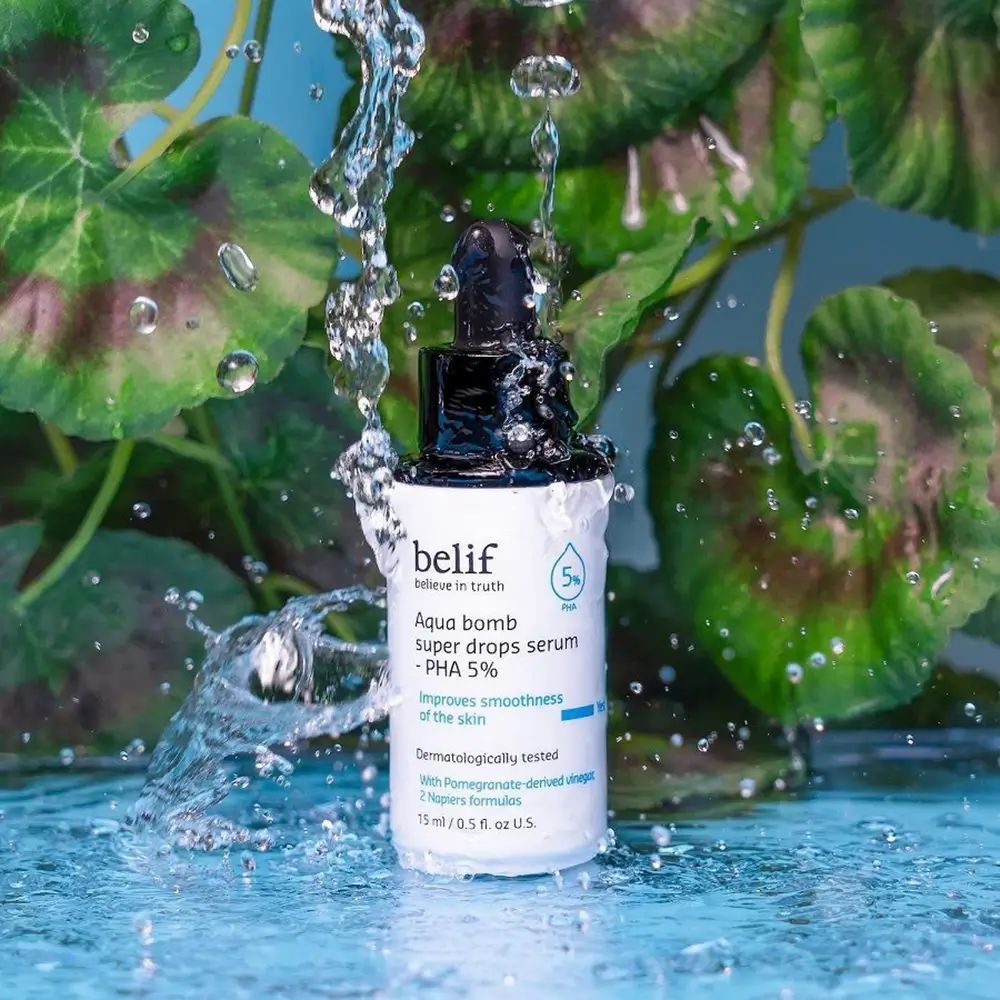 Serumflasche mit schwarzem Deckel und Pipette, umgeben von Wasser. Aufschrift: belif, Aqua bomb super drops serum - PHA 5%.