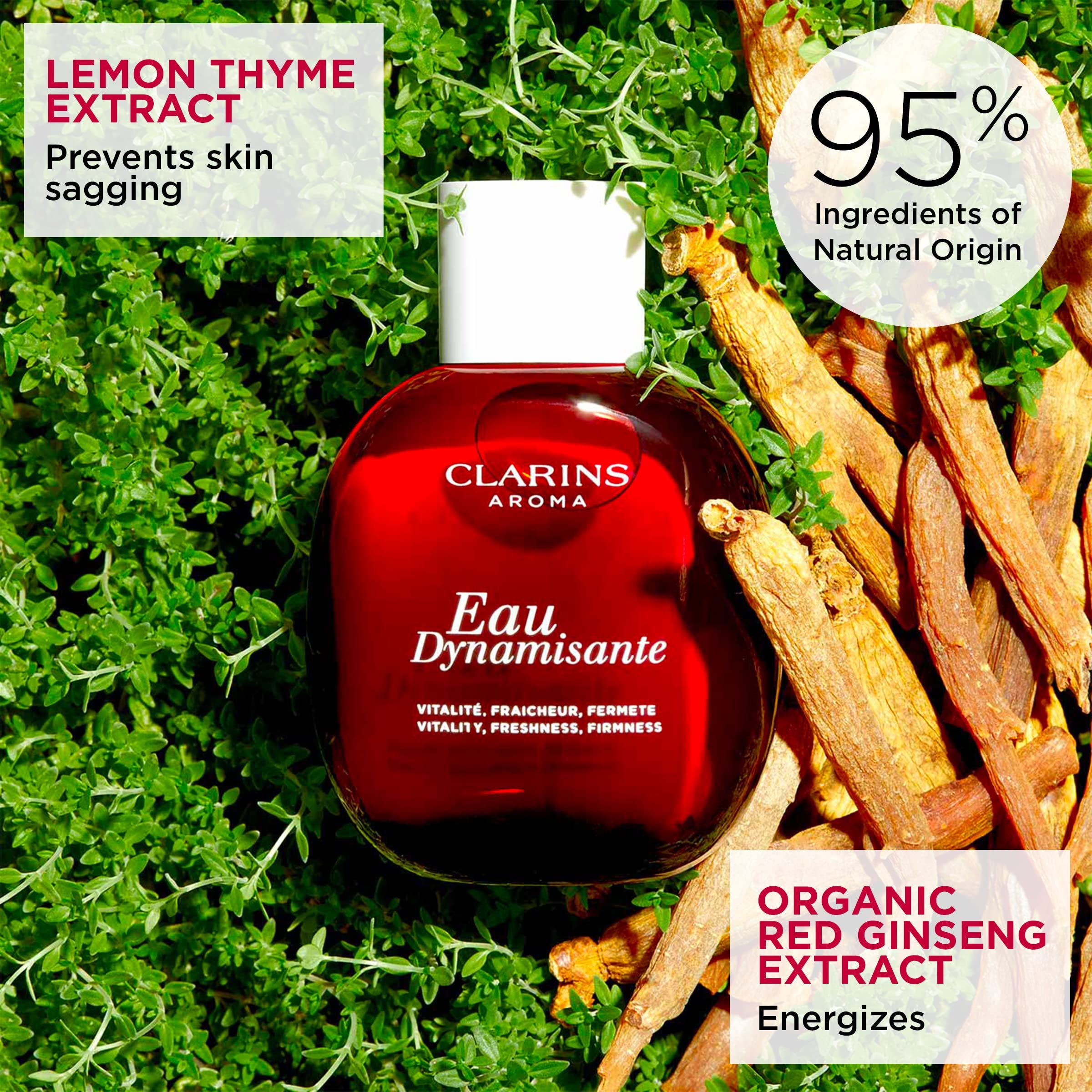 Rote Flasche Clarins Aroma Eau Dynamisante, umgeben von Kräutern und Ingwer. Text: 95% Inhaltsstoffe natürlichen Ursprungs.