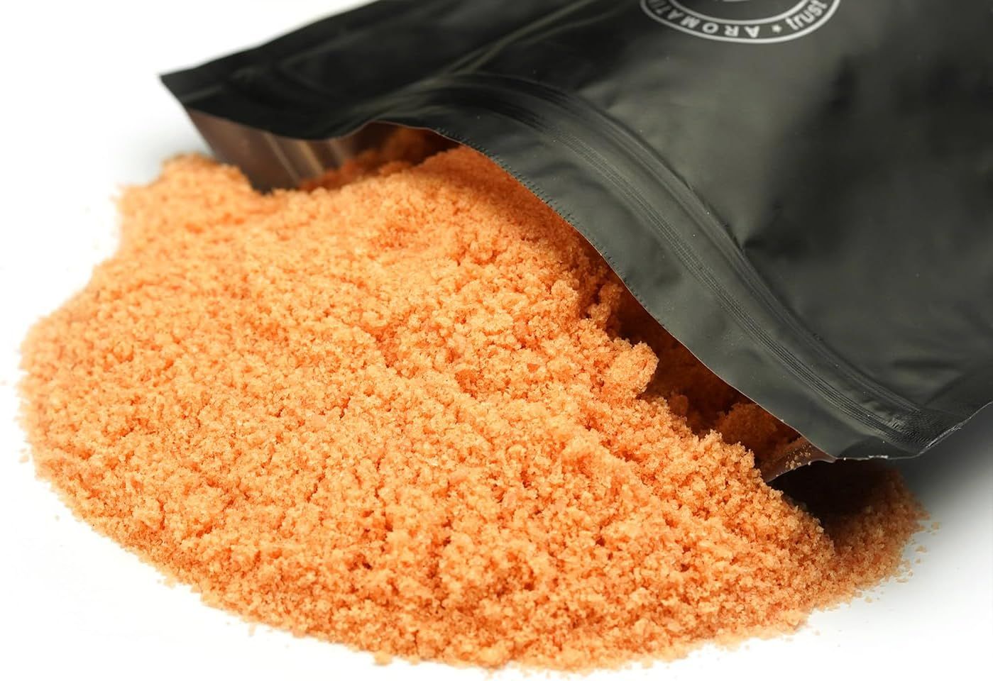 Geöffnete schwarze Verpackung. Orangefarbenes Salz liegt auf weißem Untergrund. Produktname nicht sichtbar.