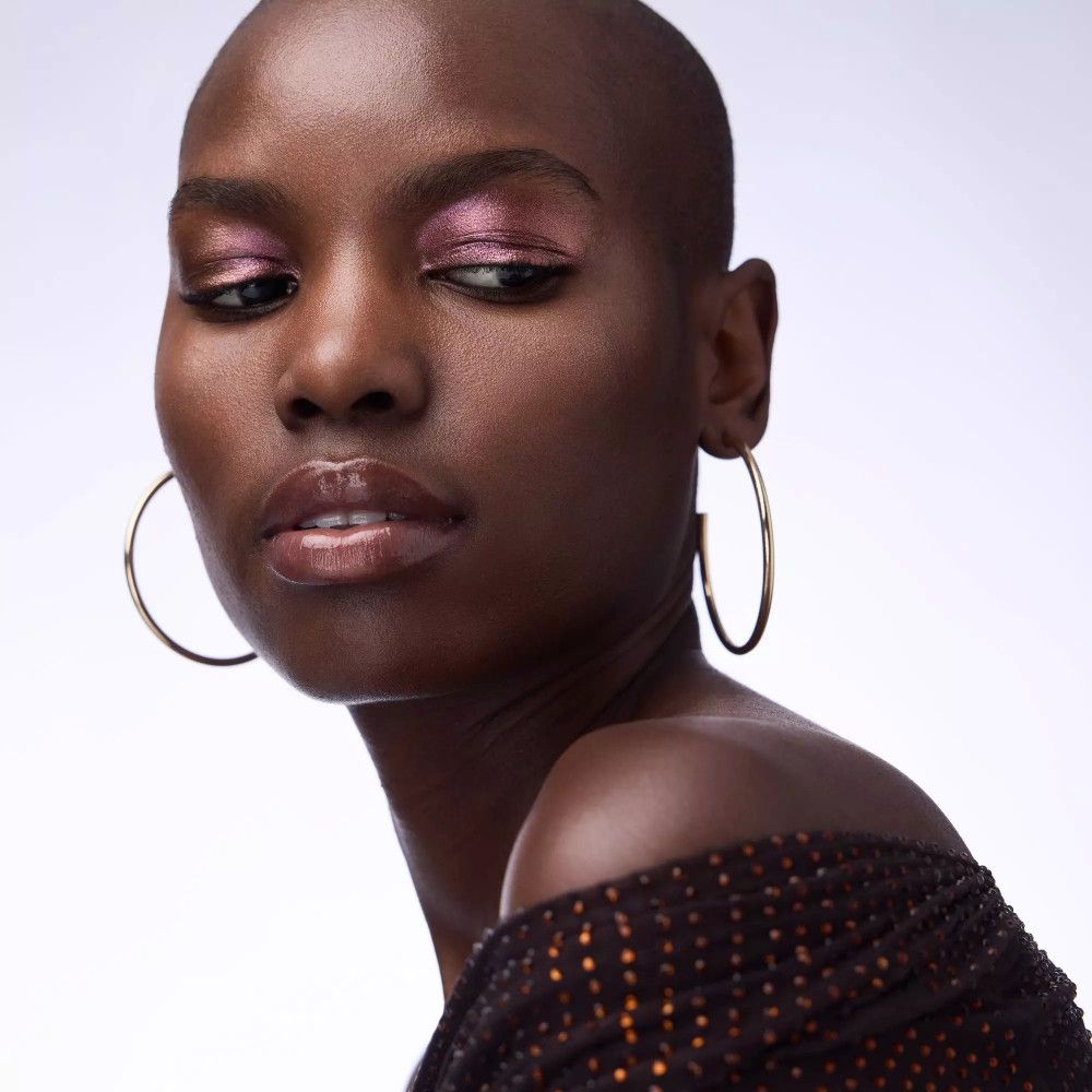 Porträt einer Frau mit rosa Lidschatten. Dunkle Haut, rasierte Haare, goldene Creolen.