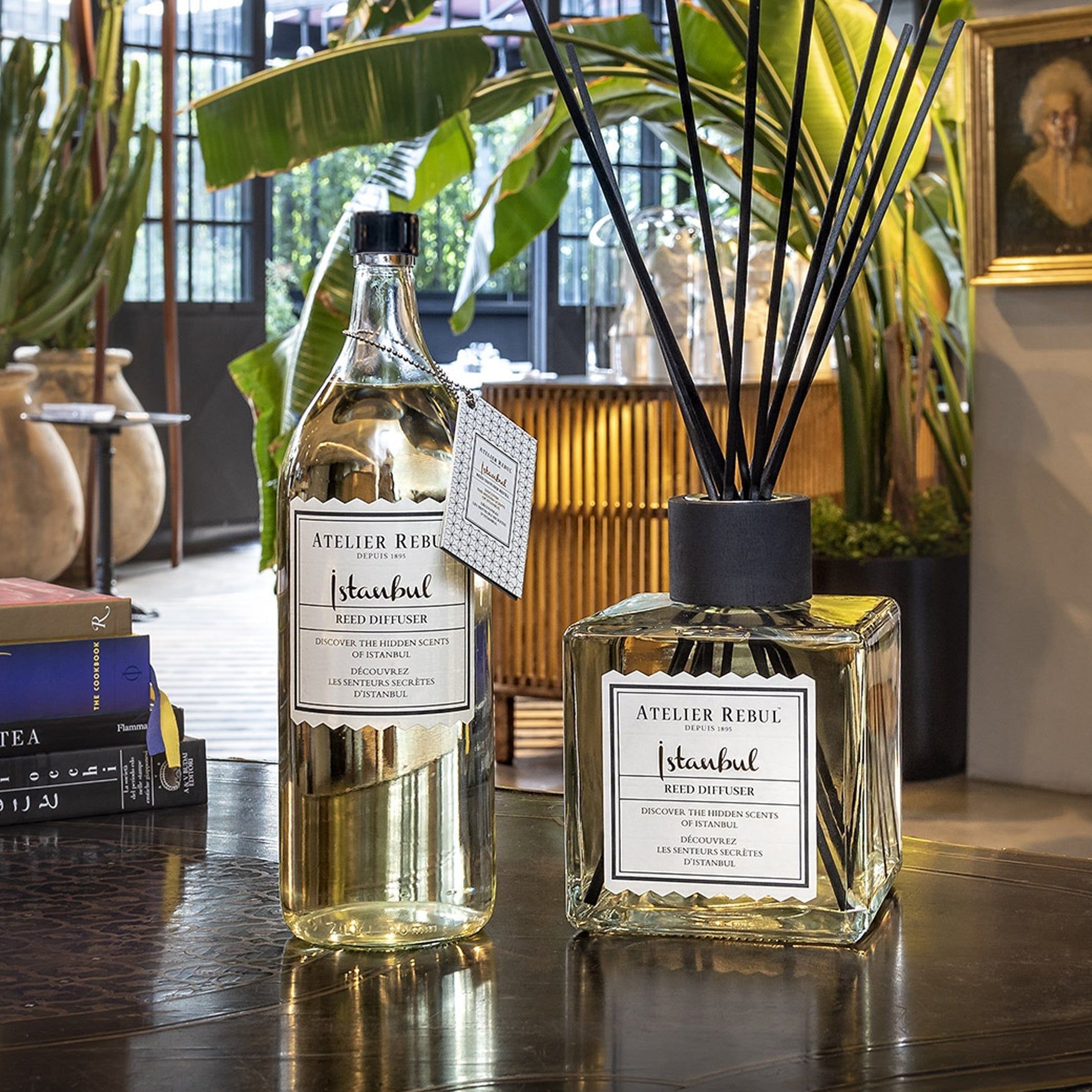 Glasflasche und quadratischer Glasdiffusor mit Stäbchen. Beide tragen das Etikett "Atelier Rebul Istanbul".