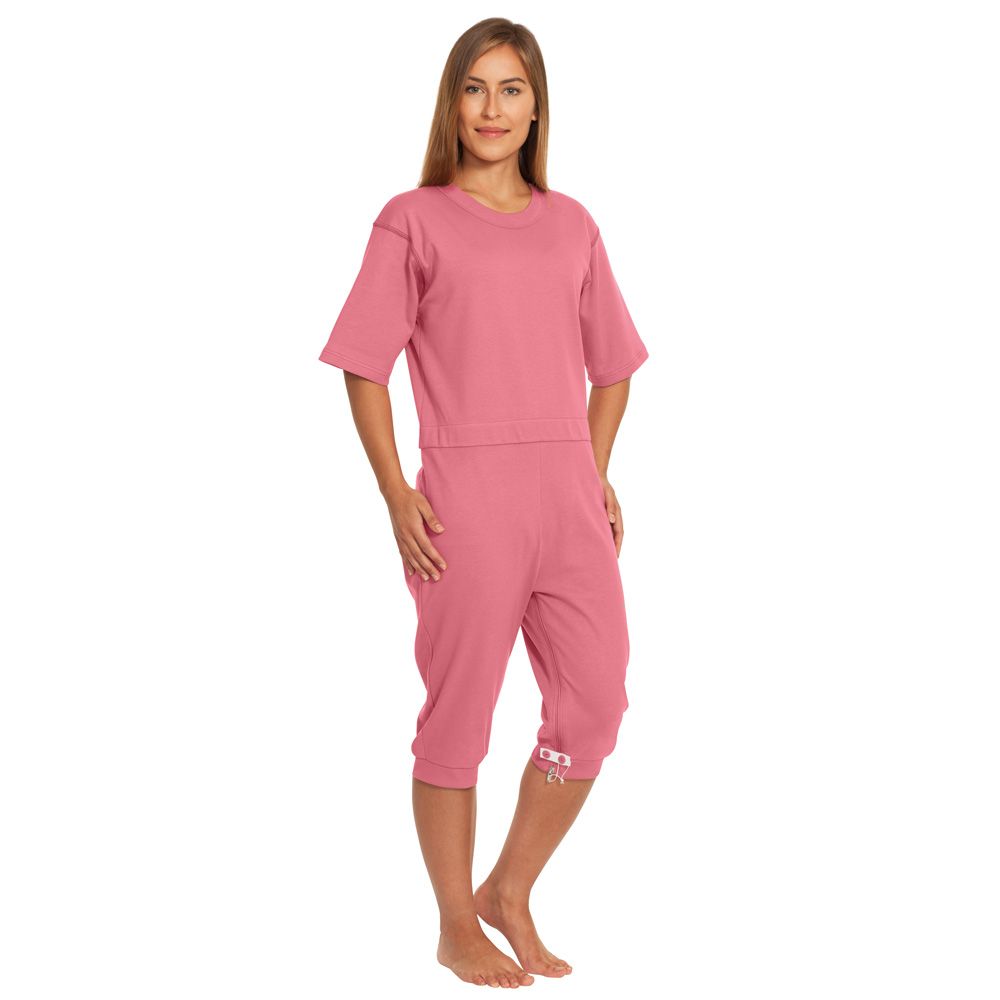 Eine Person trägt einen rosa Pflegeoverall mit kurzen Ärmeln und Knöchelbündchen. Die Person steht barfuß.