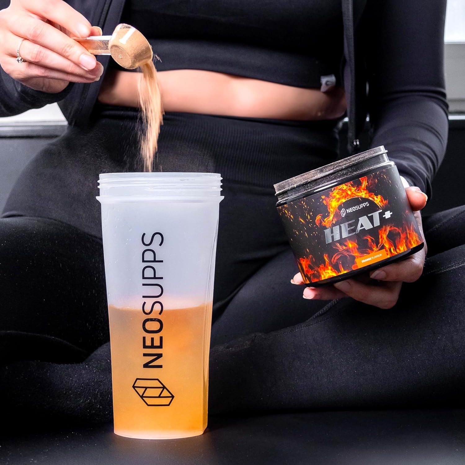 Person gießt Pulver aus Dose "HEAT+" in Shaker mit "NEOSUPPS"-Logo. Shaker teilweise gefüllt.