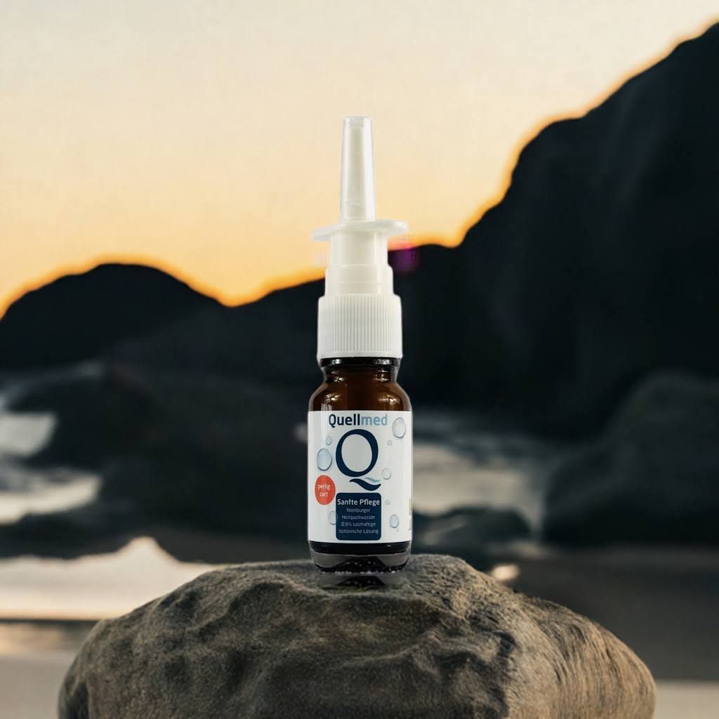 Braune Glasflasche mit weißem Sprühkopf auf einem Stein. Aufschrift: Quellmed, Sanfte Pflege. Produkt für die Nase.
