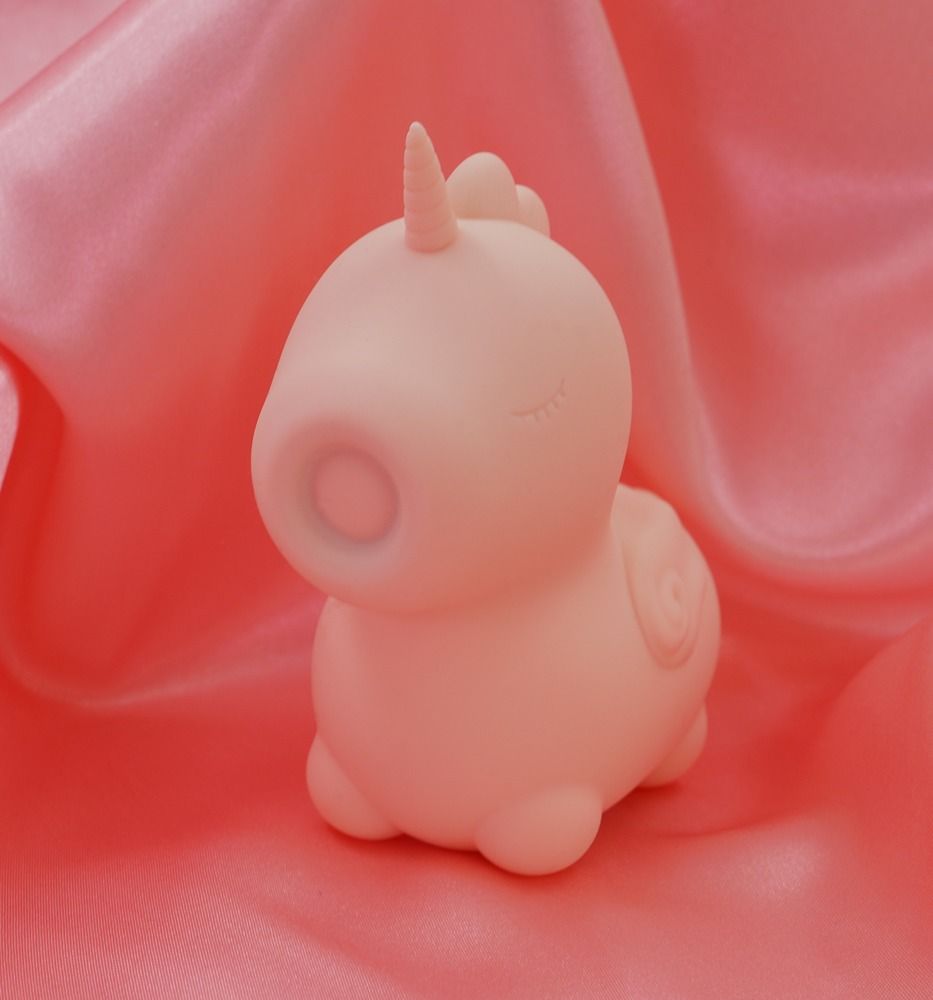 Rosa Einhorn-Vibrator. Rosa, mit geschlossenen Augen. Flügel und Horn. Auf rosa Stoff.