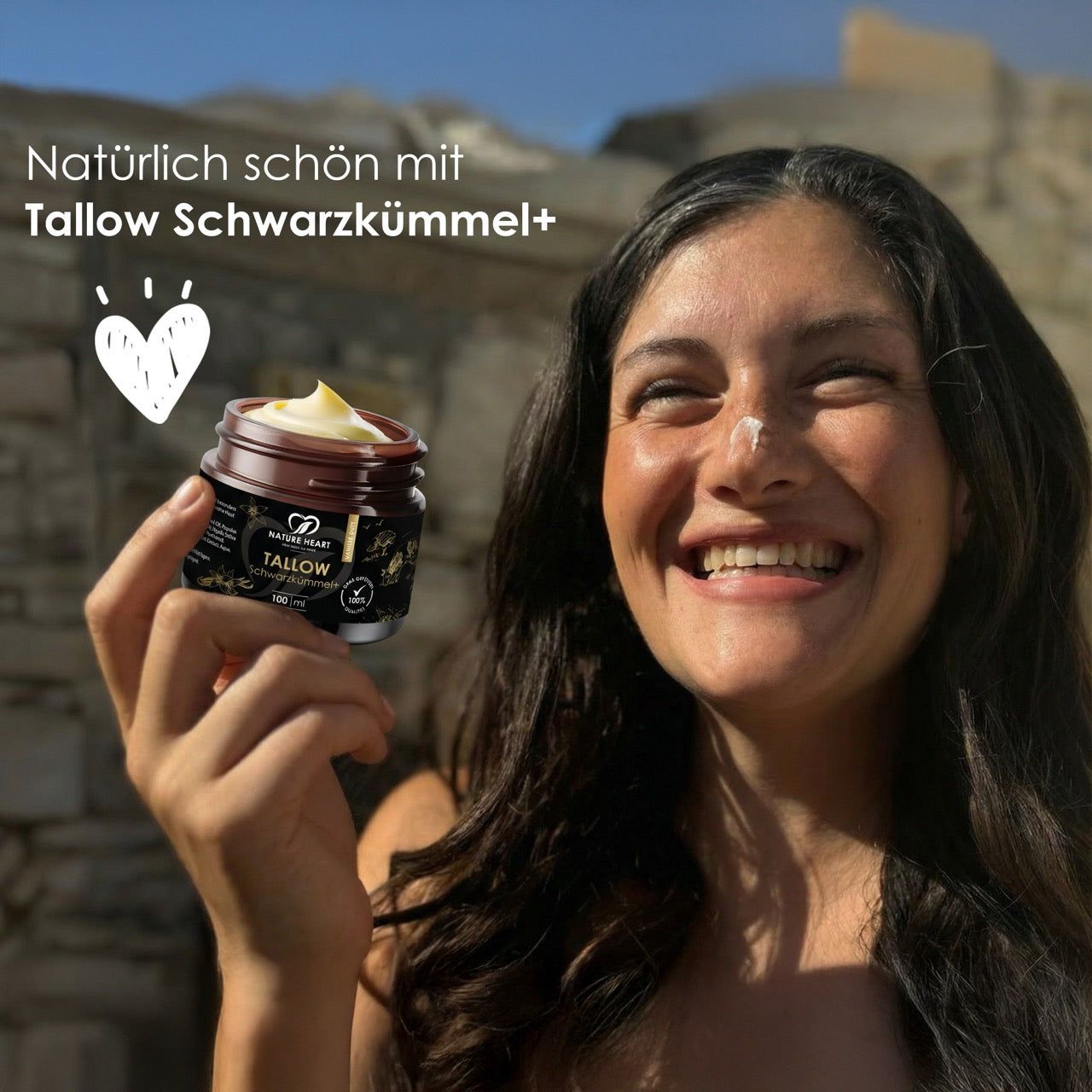 Frau lächelt, hält Dose Tallow Schwarzkümmel+. Dose mit gelblicher Creme. Text: Natürlich schön mit Tallow Schwarzkümmel+.