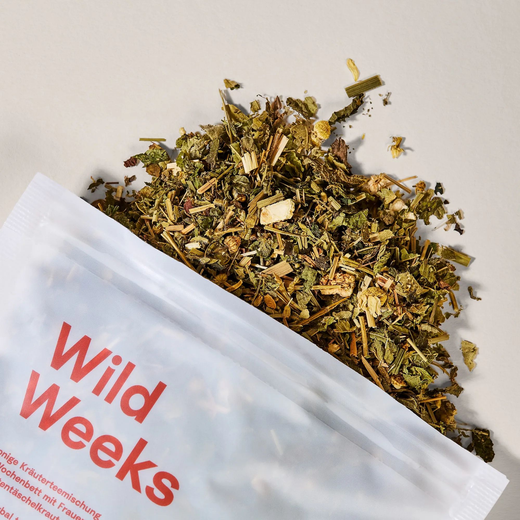 Wild Weeks Kräutermischung. Offene Kräuter neben Beutel. Text: Wochenbett-Tee, mit Frauenmantel und Hirtentäschel. Ohne Fenchel.