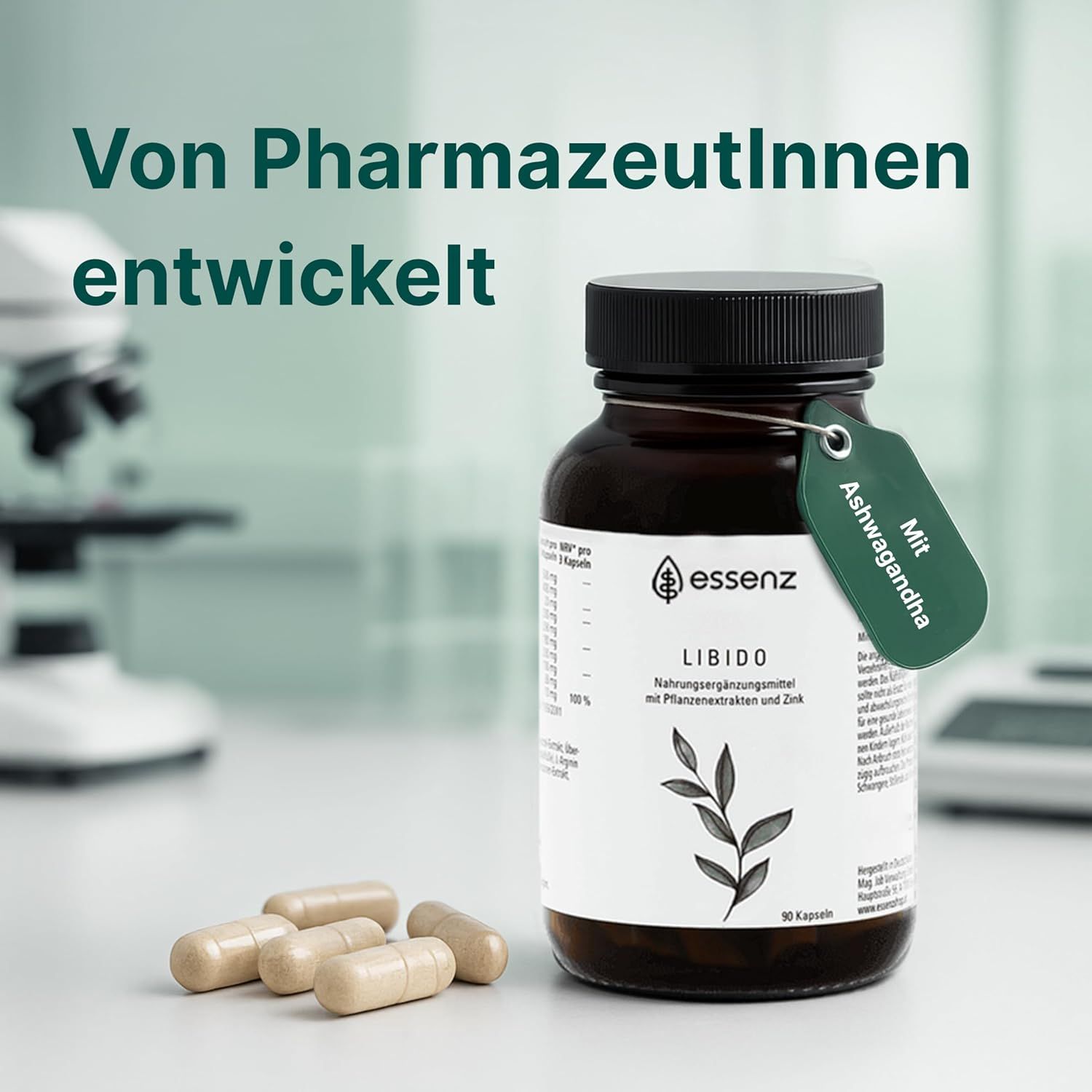 Braune Glasflasche mit ESSENZ Libido Kapseln, daneben Kapseln. Grünes Etikett mit Ashwagandha. Hintergrund: Labor.