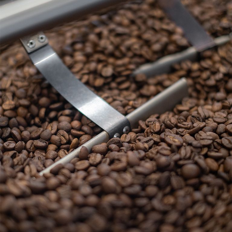 Kaffeebohnen in einer Röstmaschine. Metallarme bewegen sich durch die Bohnen. Nahaufnahme.