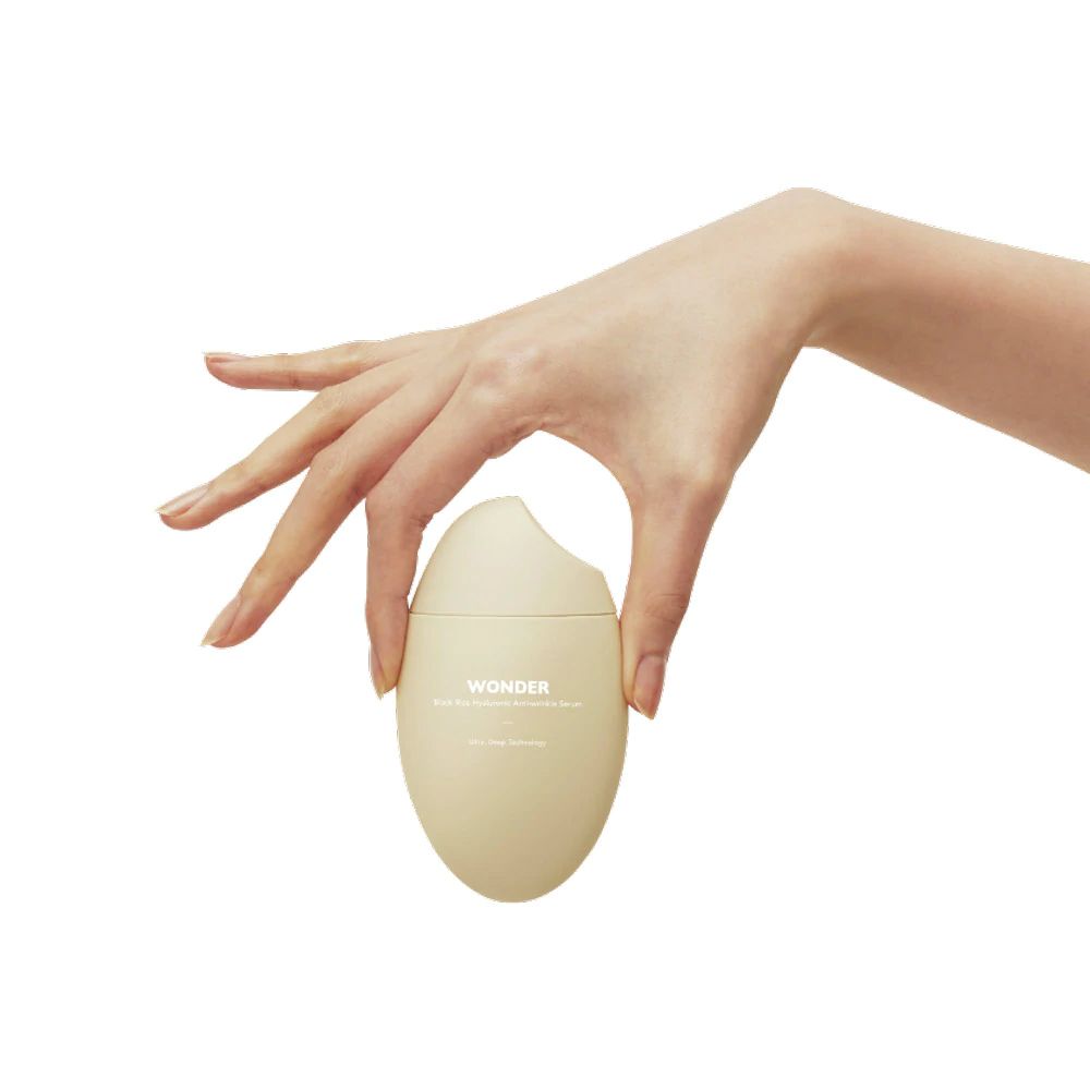 Hand hält HaruHaru Wonder Serumflasche, beige, eiförmig. Weiße Kappe, Text auf dem Flakon.