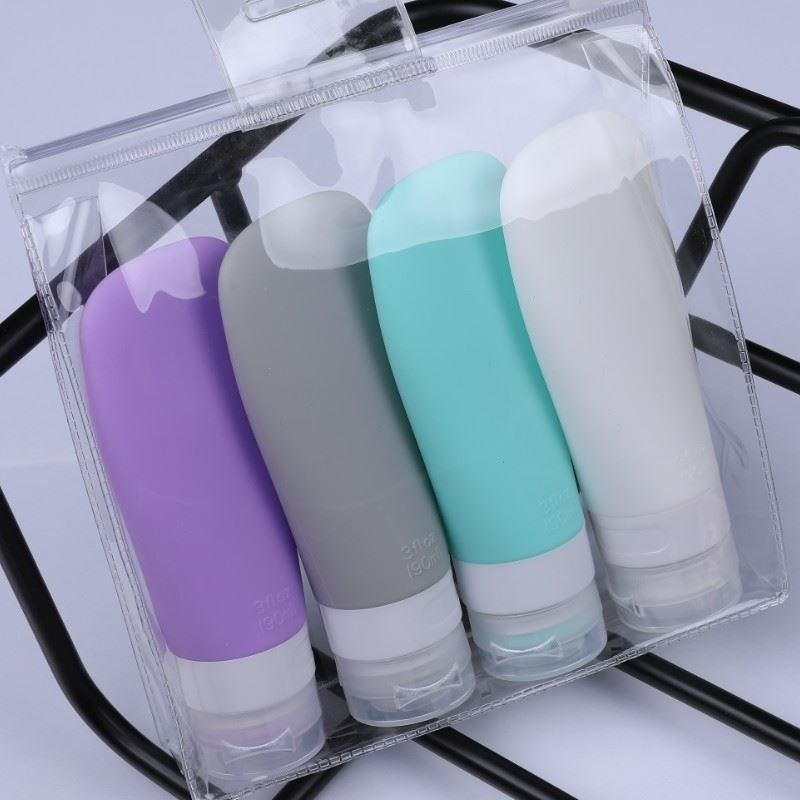 Vier farbige, wiederverwendbare Reiseflaschen in einer transparenten Tasche. Verschiedene Farben: Lila, Grau, Türkis und Weiß.