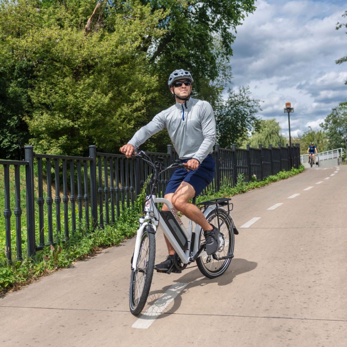 Weißes E-Bike auf Radweg. Fahrer mit Helm. JOBOBIKE-Logo nicht sichtbar.