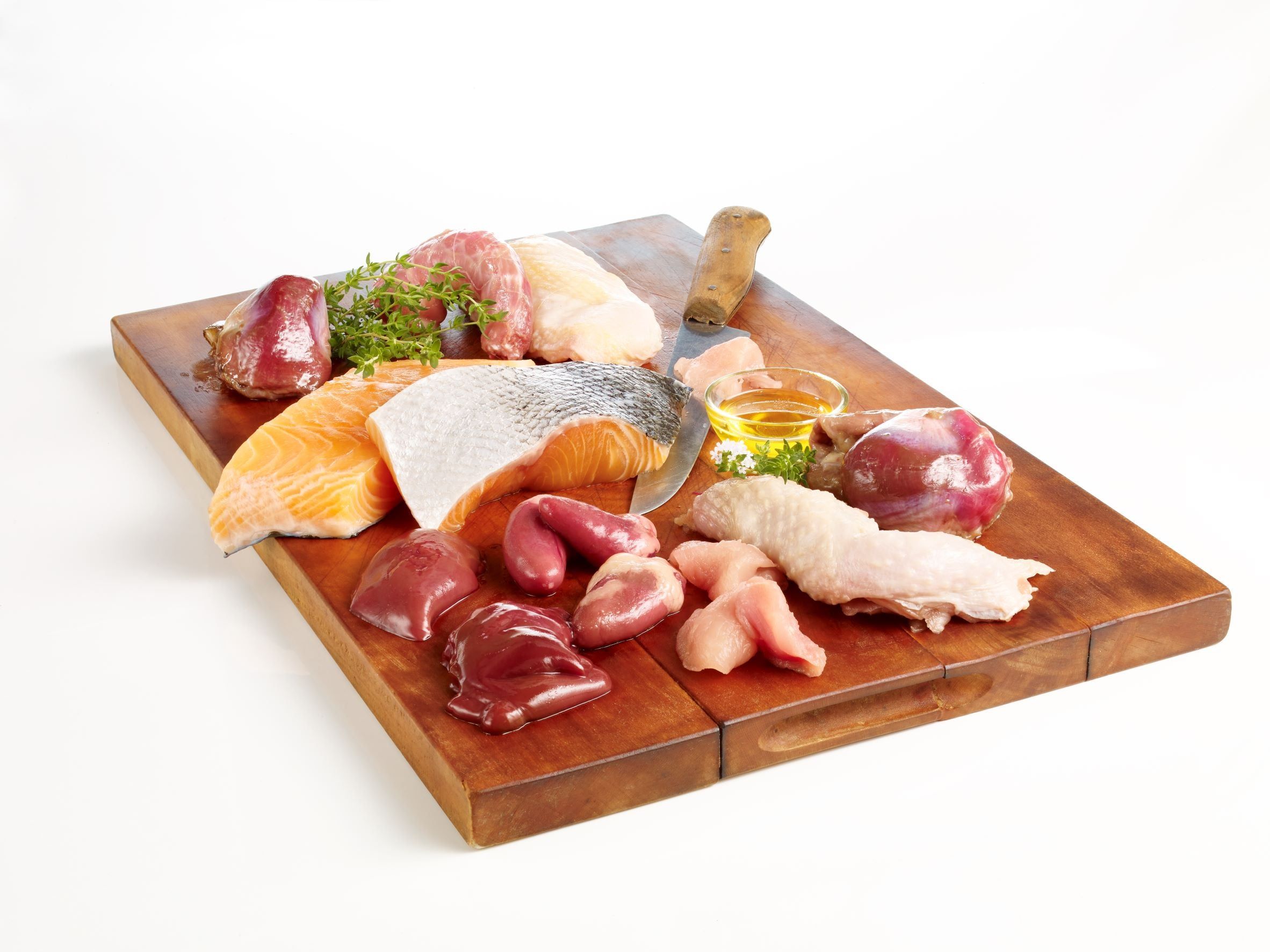 Holzbrett mit verschiedenen rohen Zutaten: Lachs, Hühnchen, Innereien, Gemüse. Auf weißem Hintergrund.