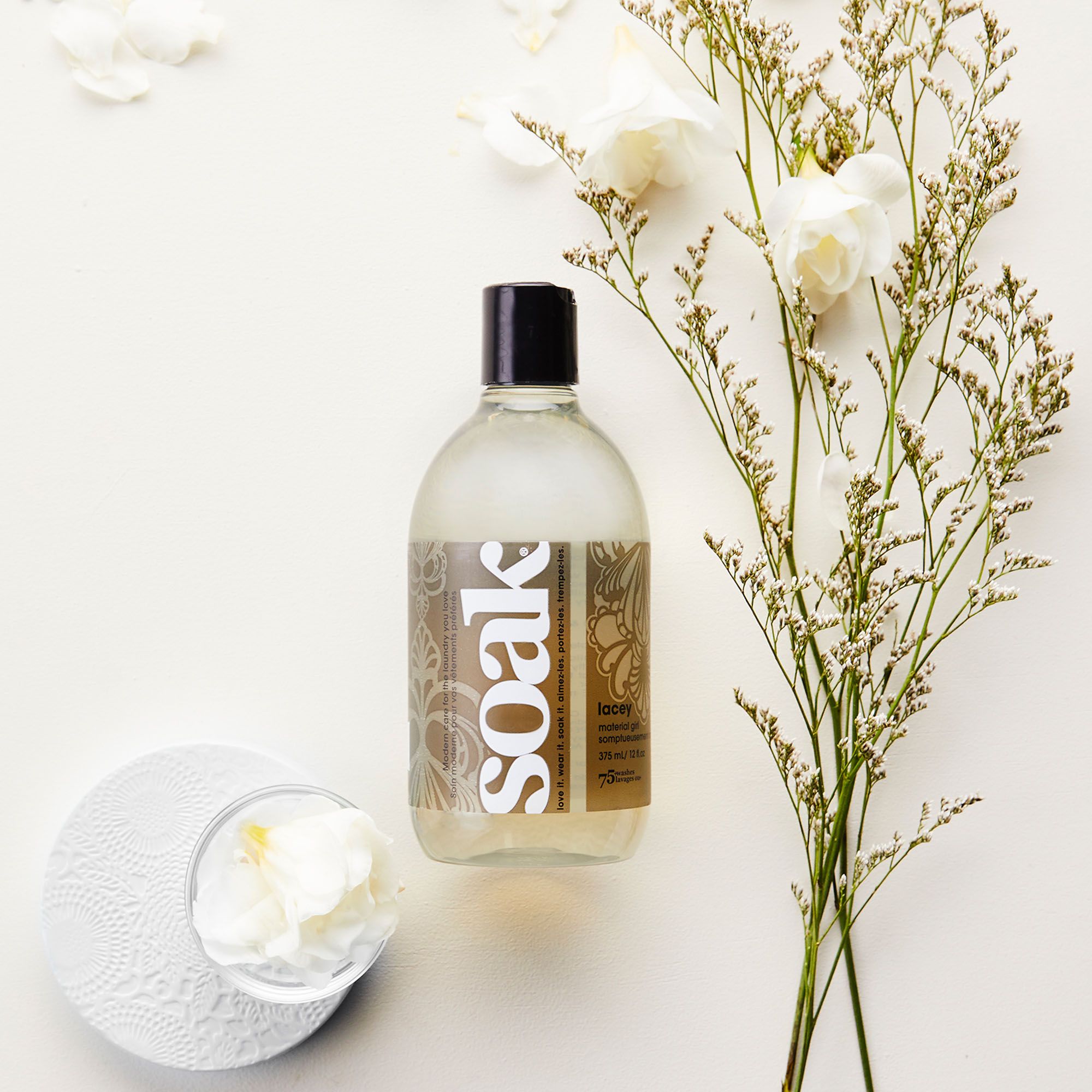 Klare Flüssigkeit in einer Flasche mit schwarzem Deckel. Aufschrift "soak". Dekorative Elemente: Blumen und Blätter.