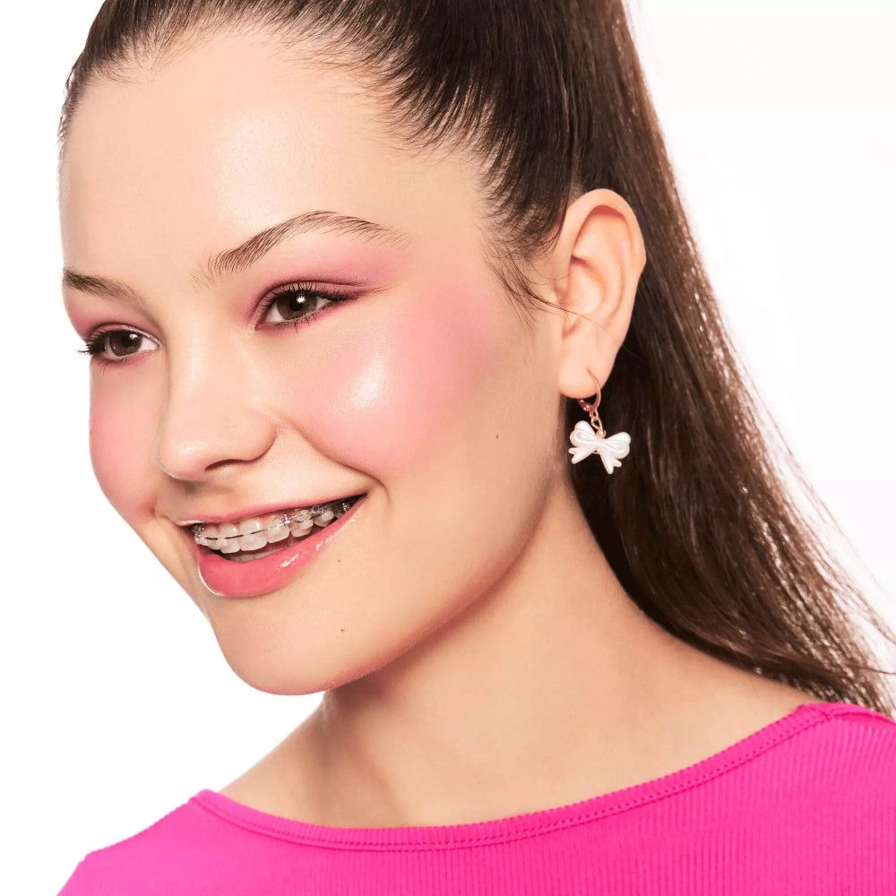 Porträt eines lächelnden Mädchens mit rosa Wangen. Sie trägt eine Zahnspange und Ohrringe in Schleifenform.