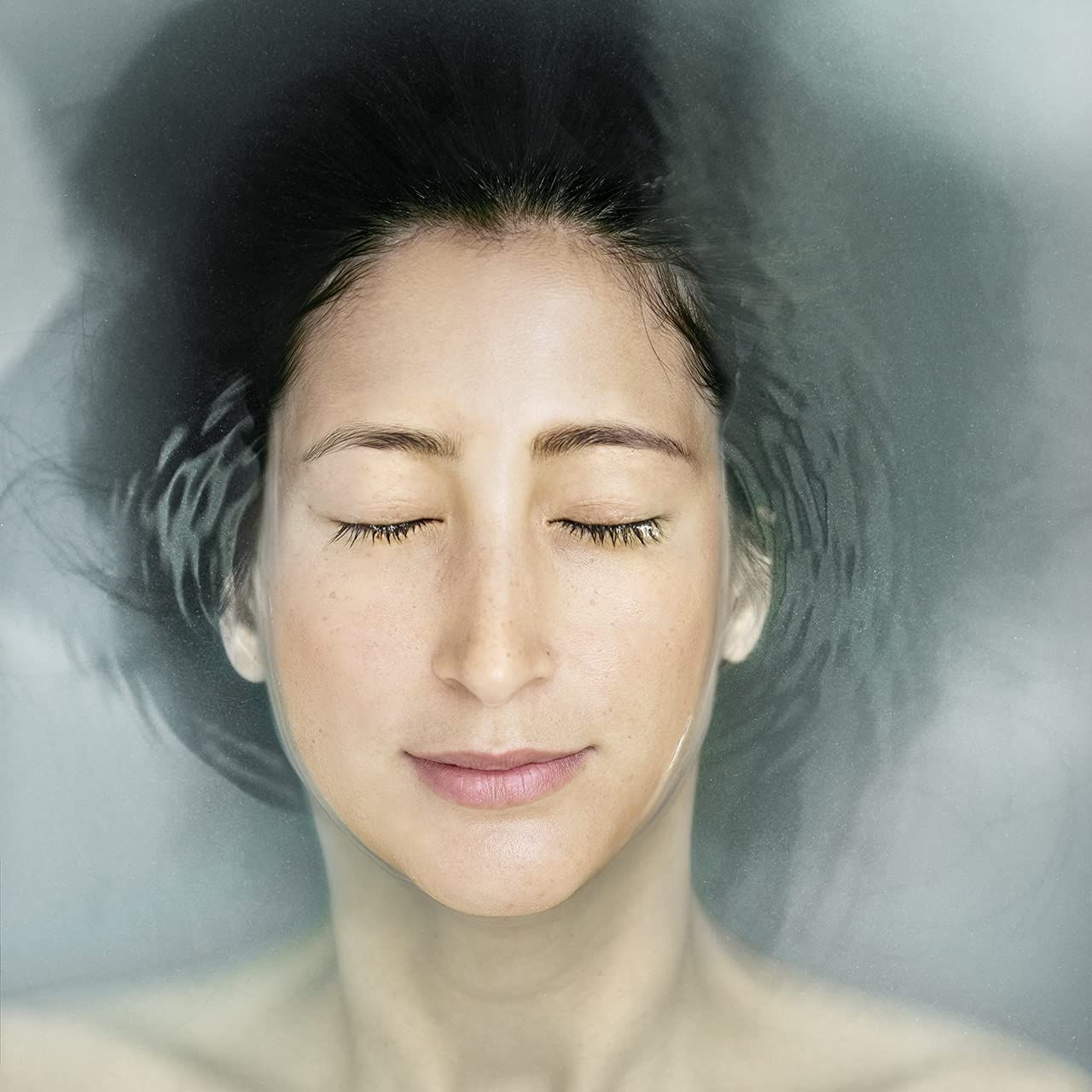 Nahaufnahme eines Gesichts unter Wasser. Augen geschlossen, entspannter Ausdruck. Wasser umgibt das Gesicht.