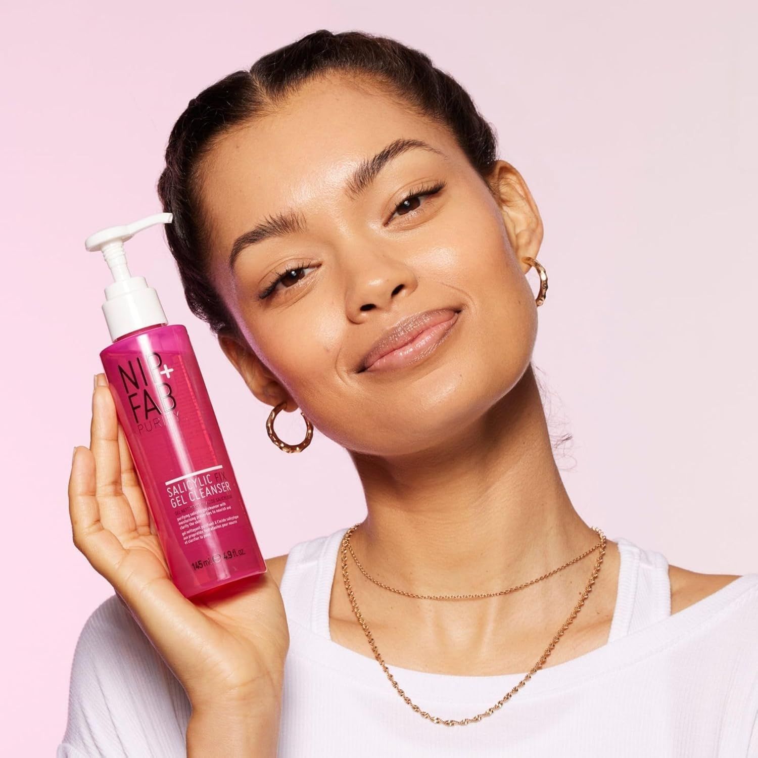 Frau hält eine rosa Flasche mit weißem Pumpkopf. Aufschrift: NIP+FAB, Salicylic Fix Gel Cleanser. Frau trägt Schmuck.