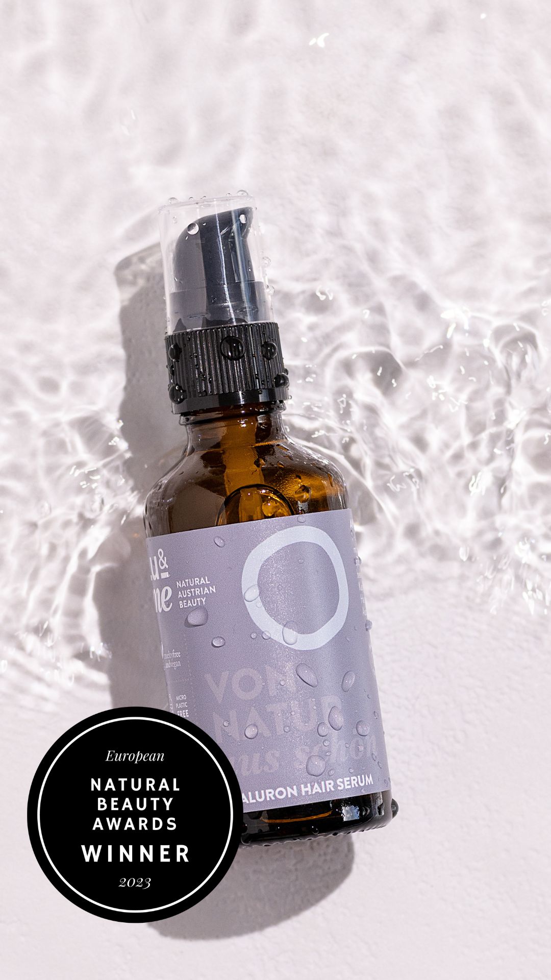 Braune Glasflasche mit Sprühkopf im Wasser. Aufkleber mit weißem Kreis und Text. Zertifizierung: Natural Beauty Awards Winner 2023.