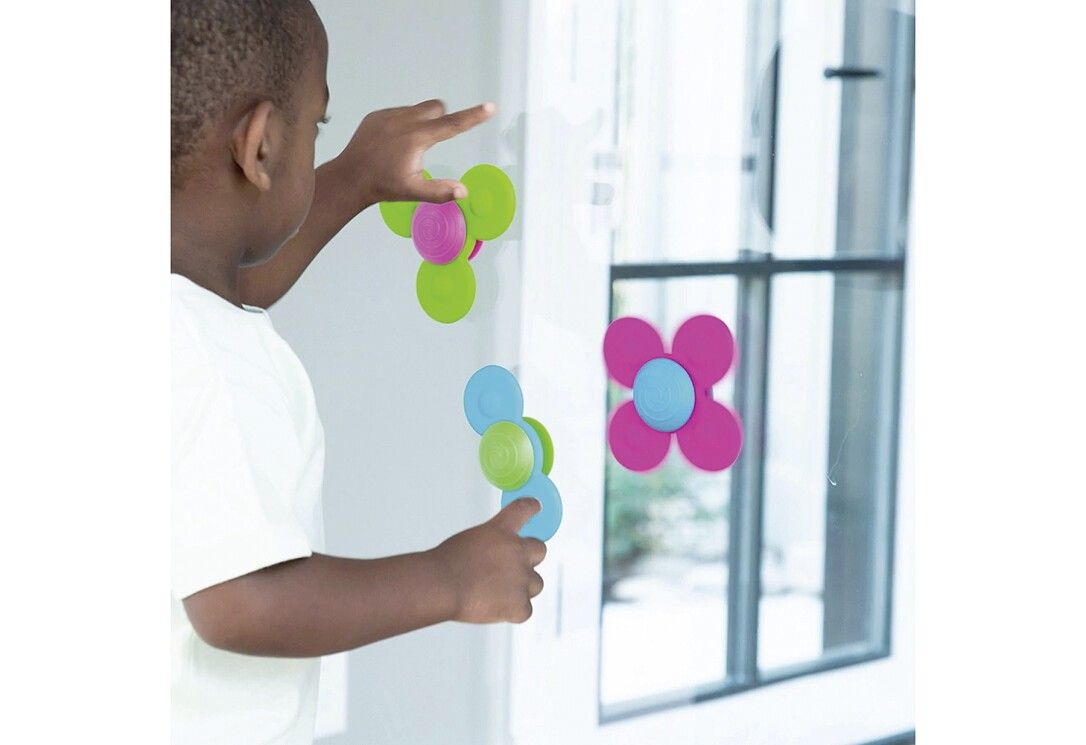 Kind hält drei bunte Spinner vor einer Glasscheibe. Die Spinner sind in Grün, Pink und Blau gehalten.