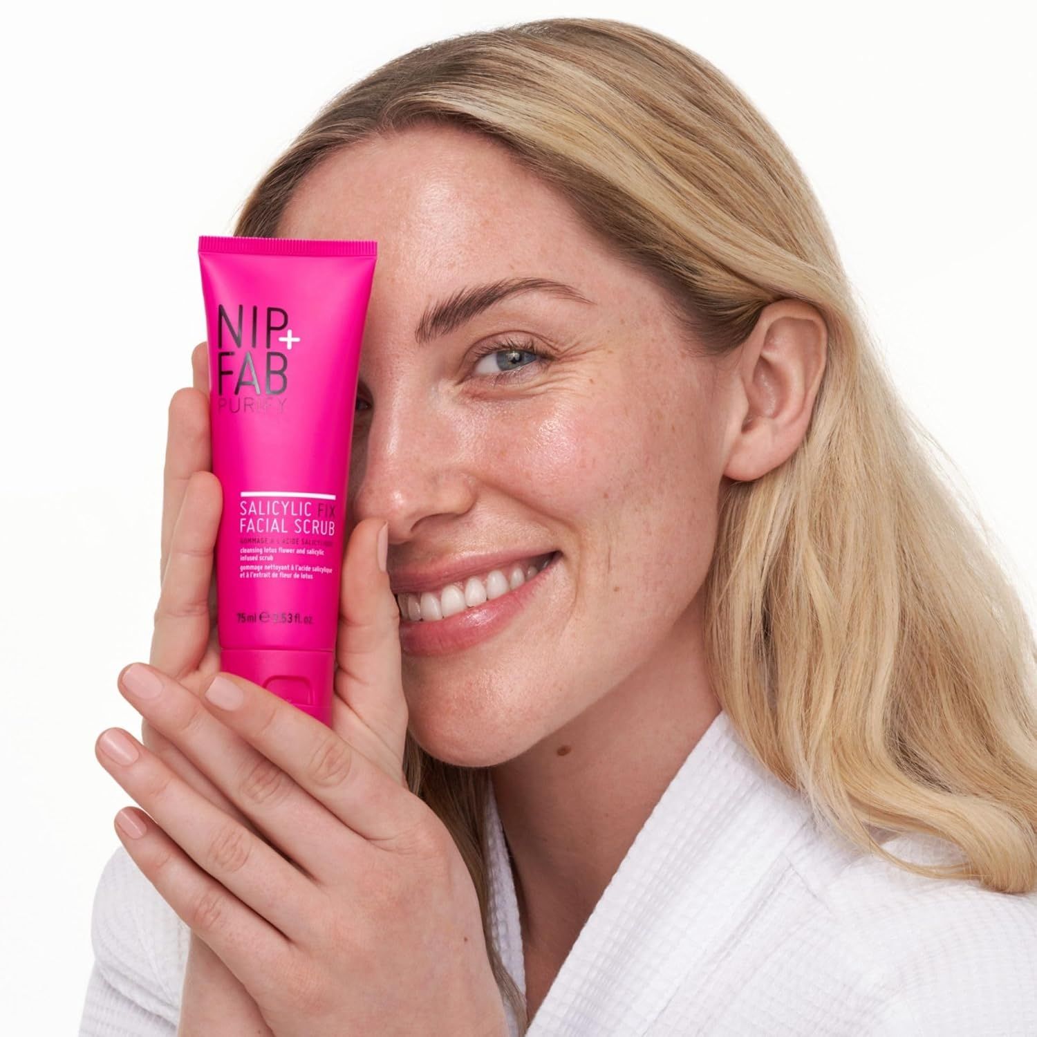 Frau hält pinkfarbene Tube vor Gesicht. Auf der Tube steht "NIP+FAB" und "SALICYLIC FACIAL SCRUB".