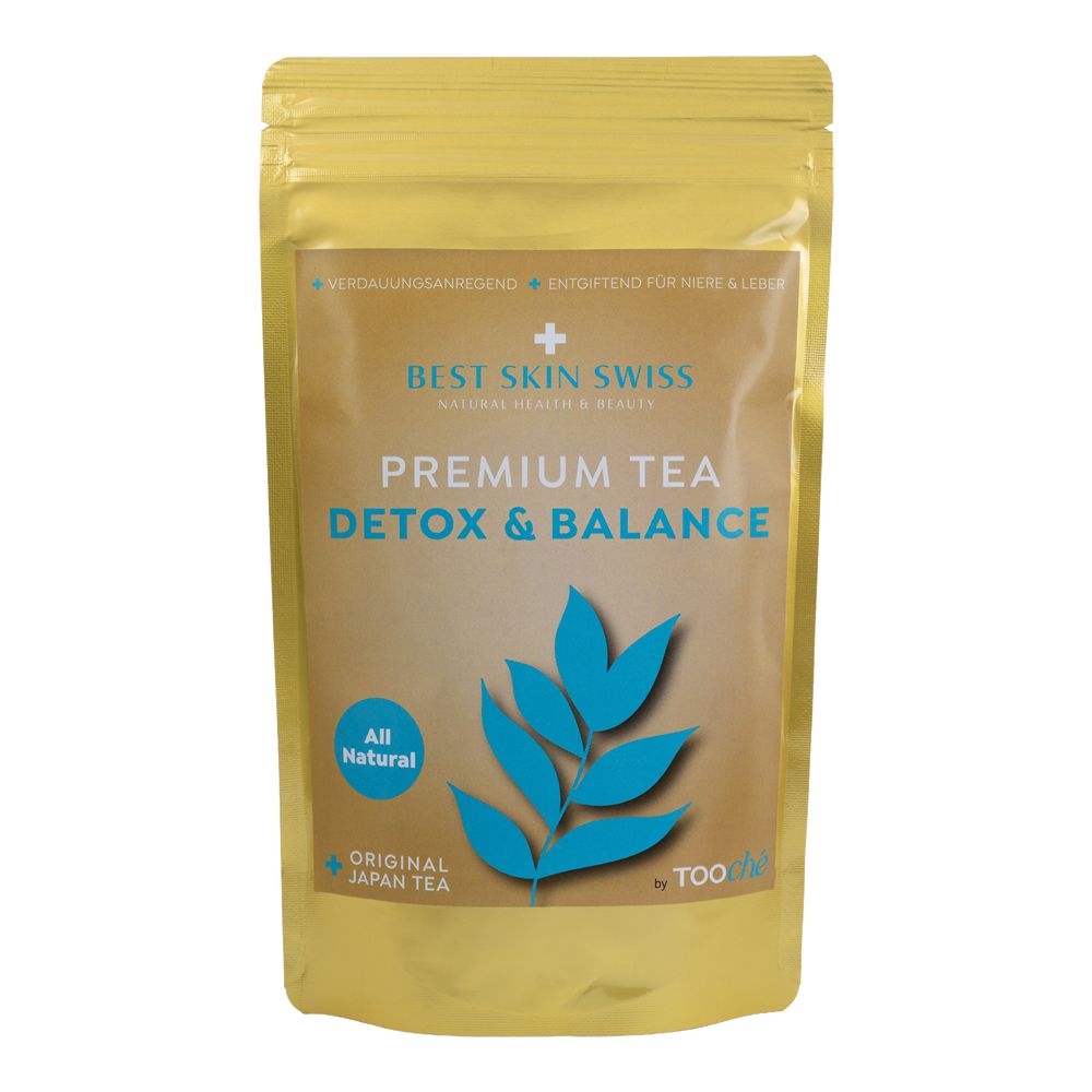 Goldfarbene Verpackung mit Aufdruck. Text: BEST SKIN SWISS PREMIUM TEA DETOX & BALANCE. Blaue Blattform. All Natural. Original Japan Tea.