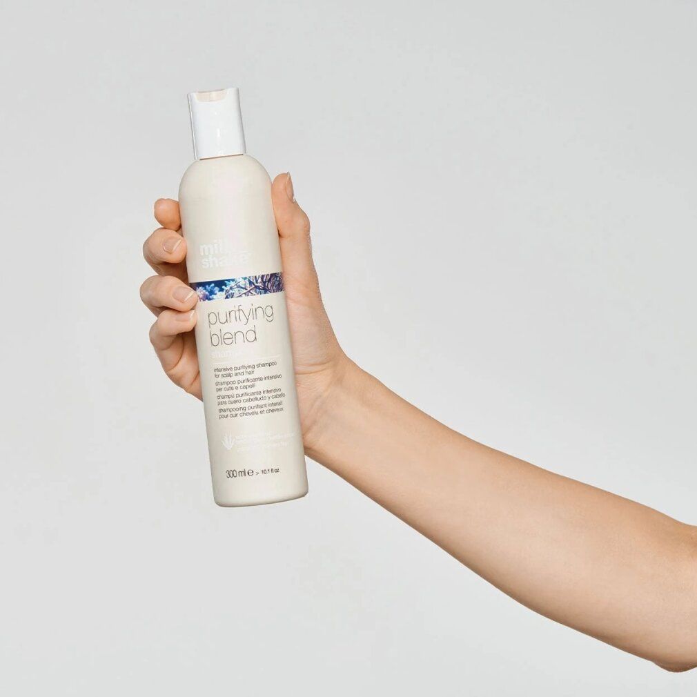 Hand hält eine beige Shampoo-Flasche mit weißem Deckel. Aufschrift: purifying blend. Text darunter: intensive purifying shampoo. Unten: 300 ml.