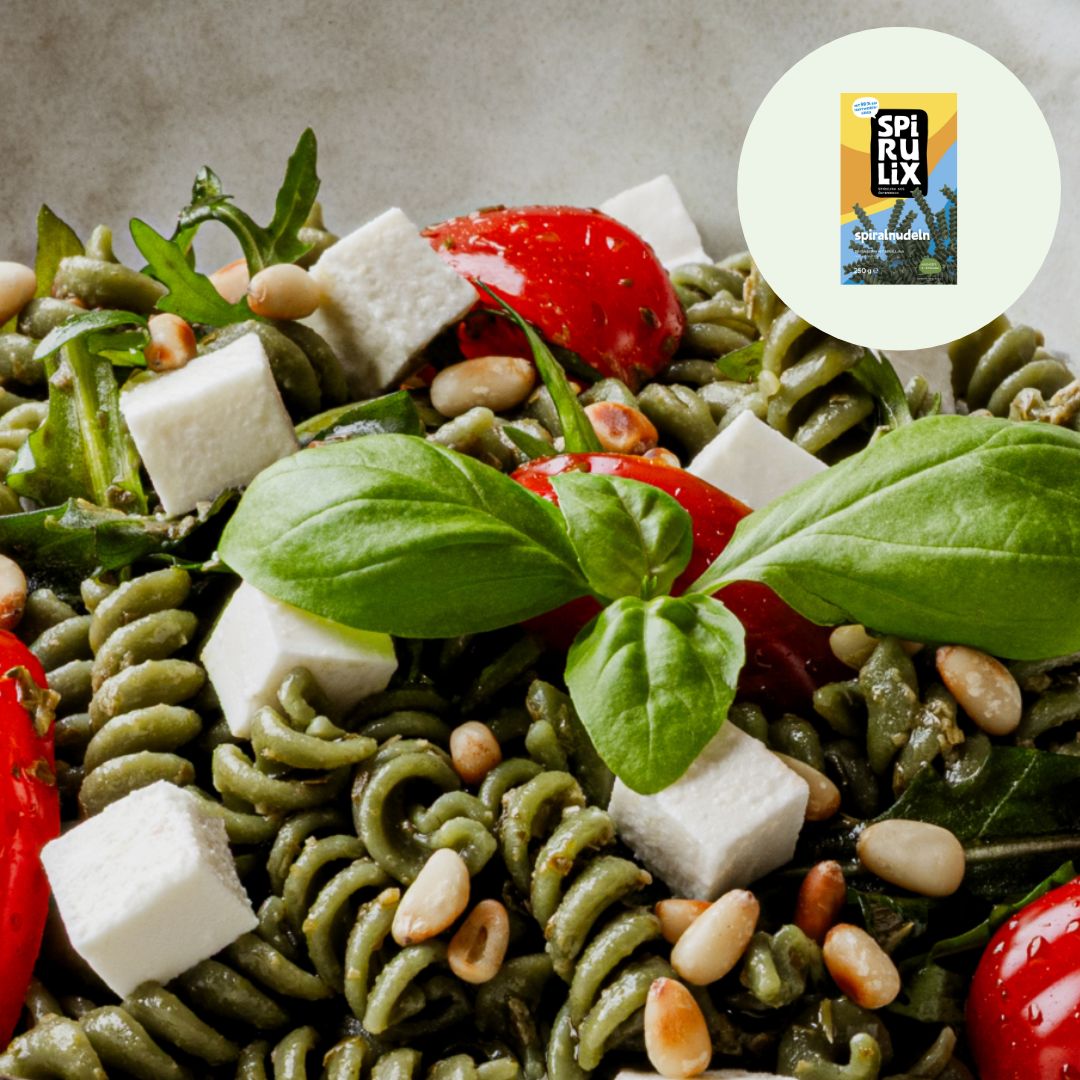 Teller mit Spirulix-Nudeln, Tomaten, Käse, Pinienkernen und Basilikum. Im Hintergrund die Spirulix-Verpackung.