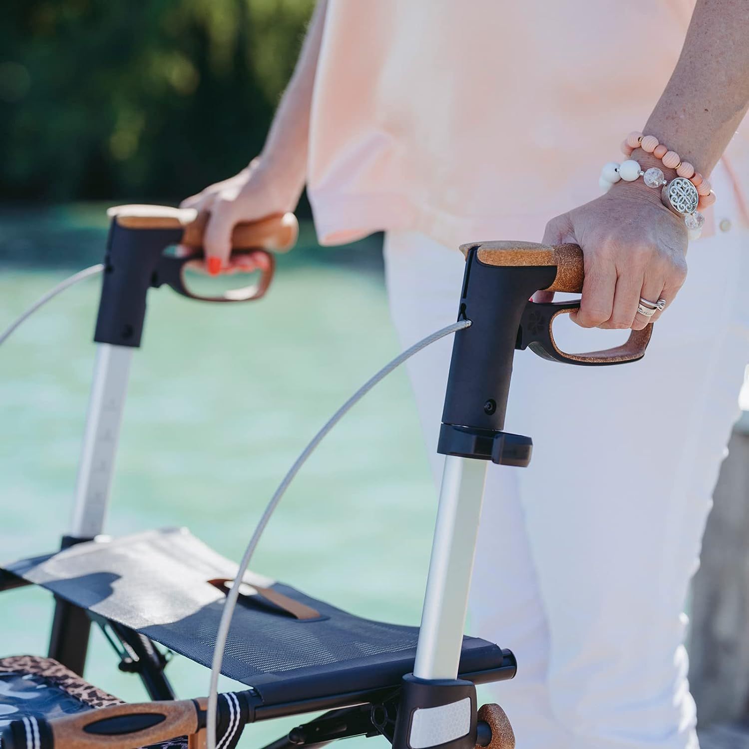 Nahaufnahme der Griffe eines Rollators. Die Griffe sind braun und an einem silbernen Rahmen befestigt.