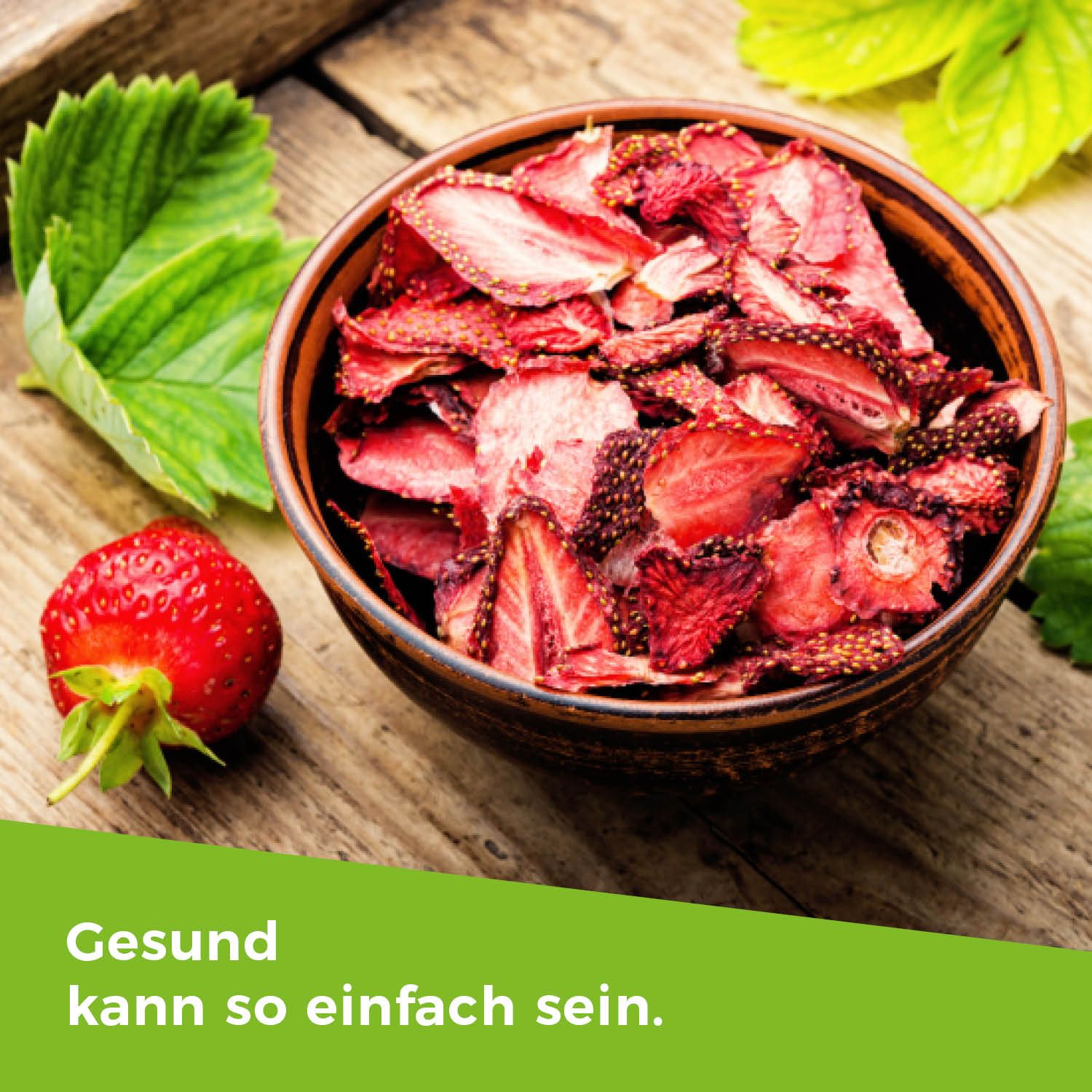 Schale mit gefriergetrockneten Erdbeerscheiben. Daneben eine frische Erdbeere. Text: Gesund kann so einfach sein.