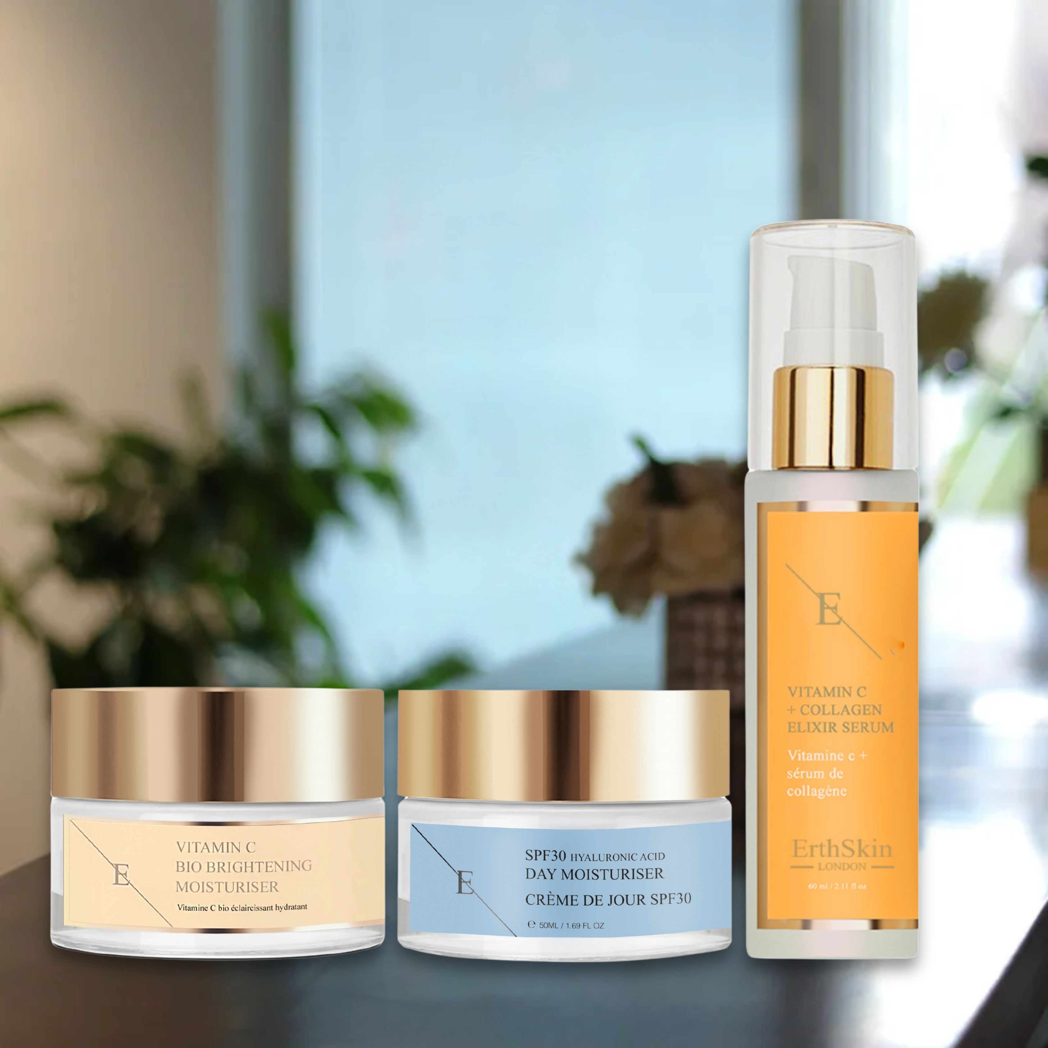 Drei Kosmetikprodukte: Serum, Tagescreme und Feuchtigkeitspflege. Goldfarbene Deckel, transparente Behälter, Etiketten mit Text. Auf Tisch platziert.