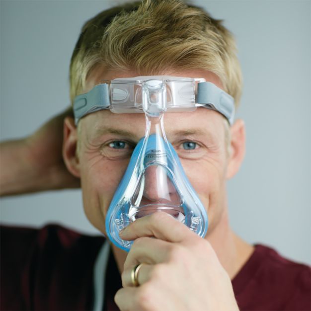 Mann mit Philips CPAP Maske Amara SE Gel Full: Mund-Nasenmaske wird angepasst.