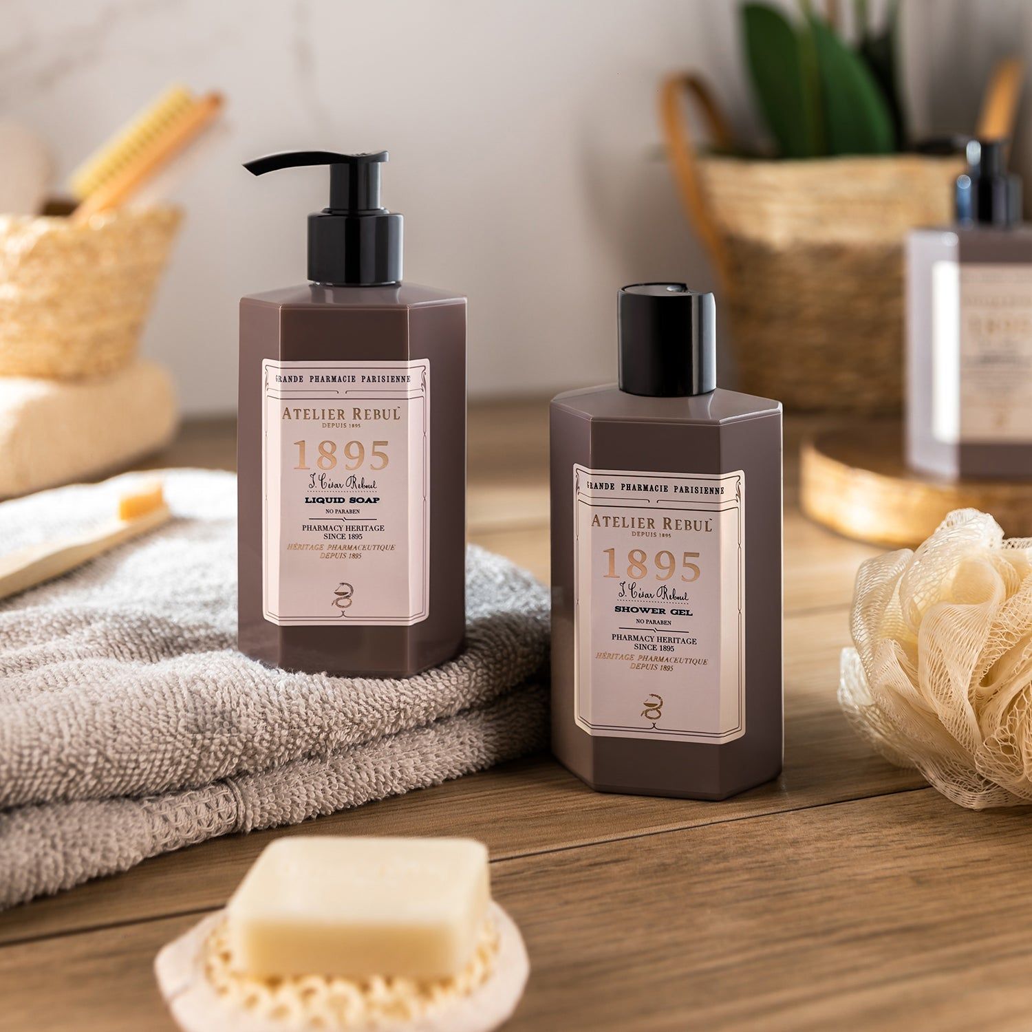 Zwei braune Flaschen mit schwarzem Pumpkopf. Aufschrift: Atelier Rebul 1895 Liquid Soap. Auf einem Handtuch und Seife.