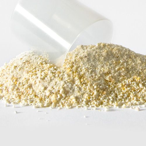 Haufen von pulverförmigem Produkt mit einem Messbecher. Das Produkt ist hellgelb und körnig. Der Becher ist durchsichtig.