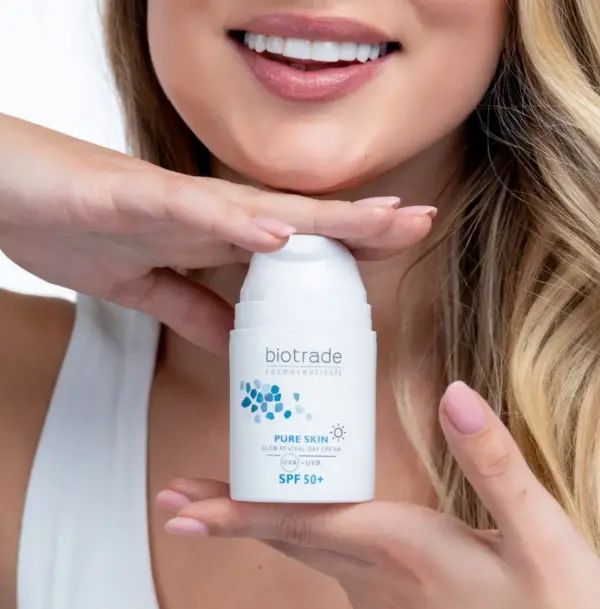 Frau hält eine weiße Creme-Flasche. Aufschrift: Biotrade, Pure Skin, SPF 50+. Frau lächelt.