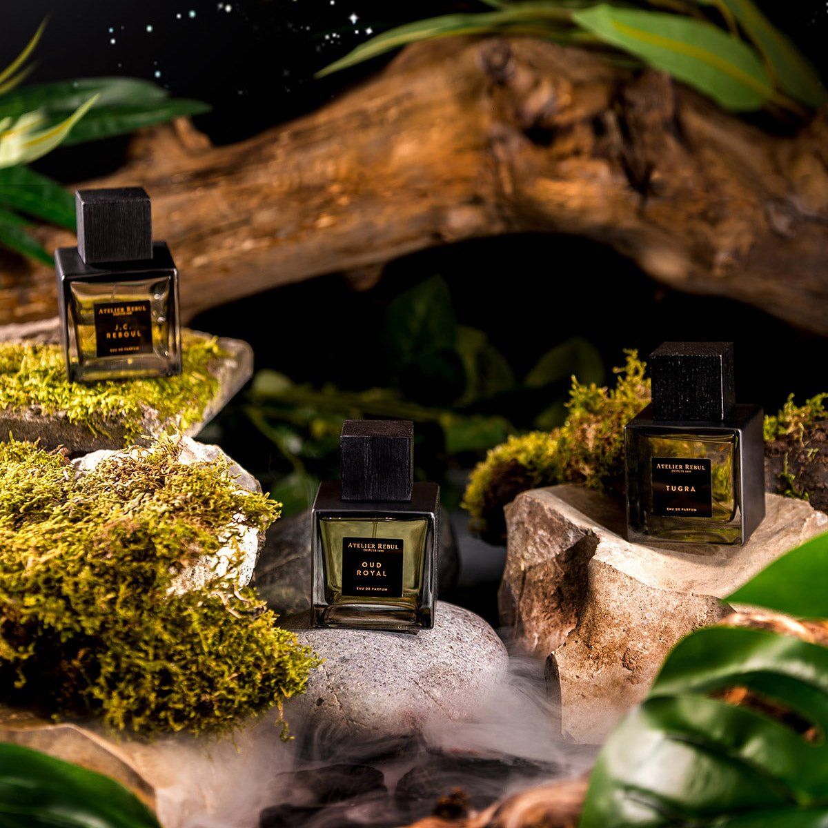 Drei Parfümflakons auf Steinen und Moos. Auf den Etiketten steht "OUD ROYAL", "LE DESIR" und "TUGRA".