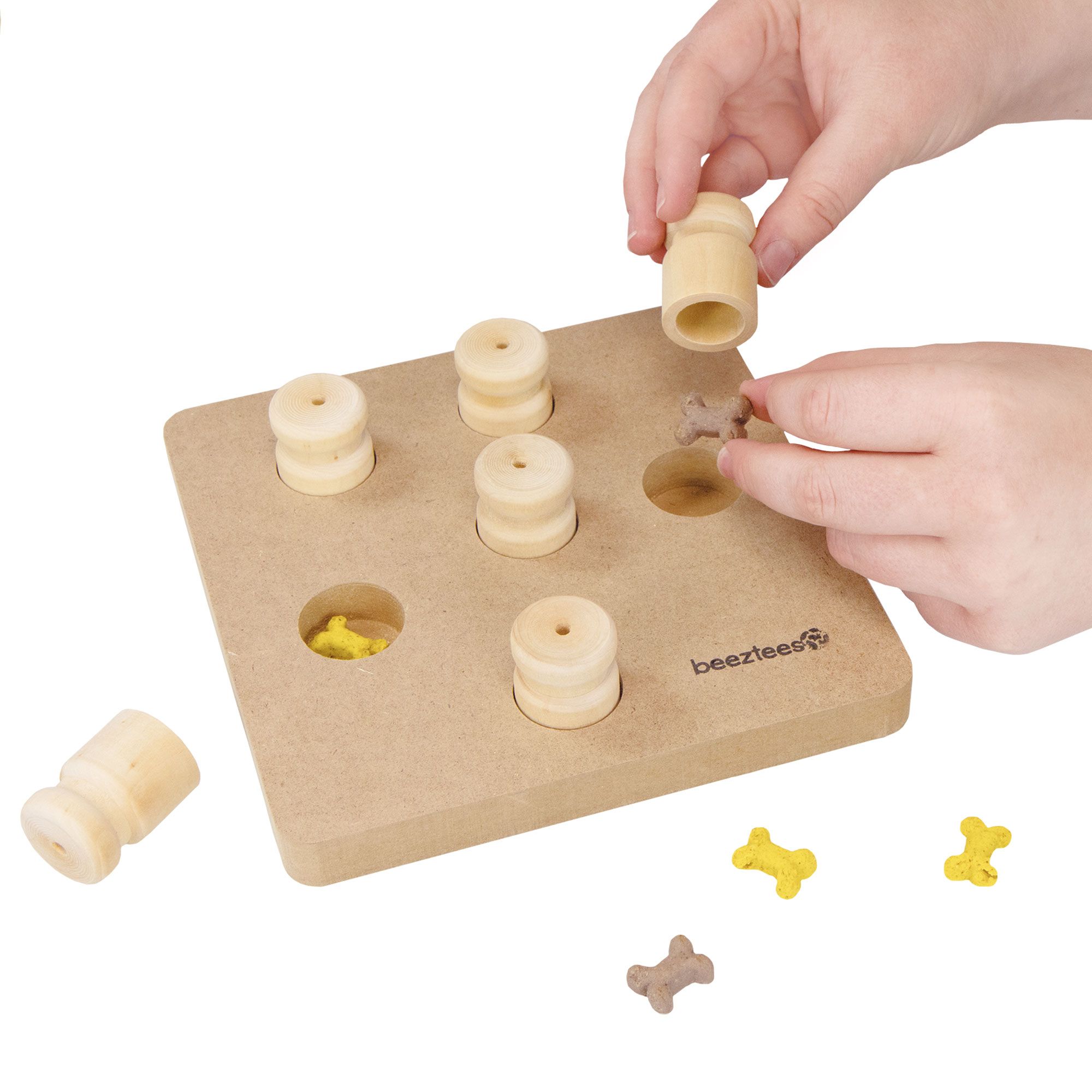 Holzbrett mit Stiften, Knochen und Stiften daneben. Hände interagieren. Marke Beeztees.