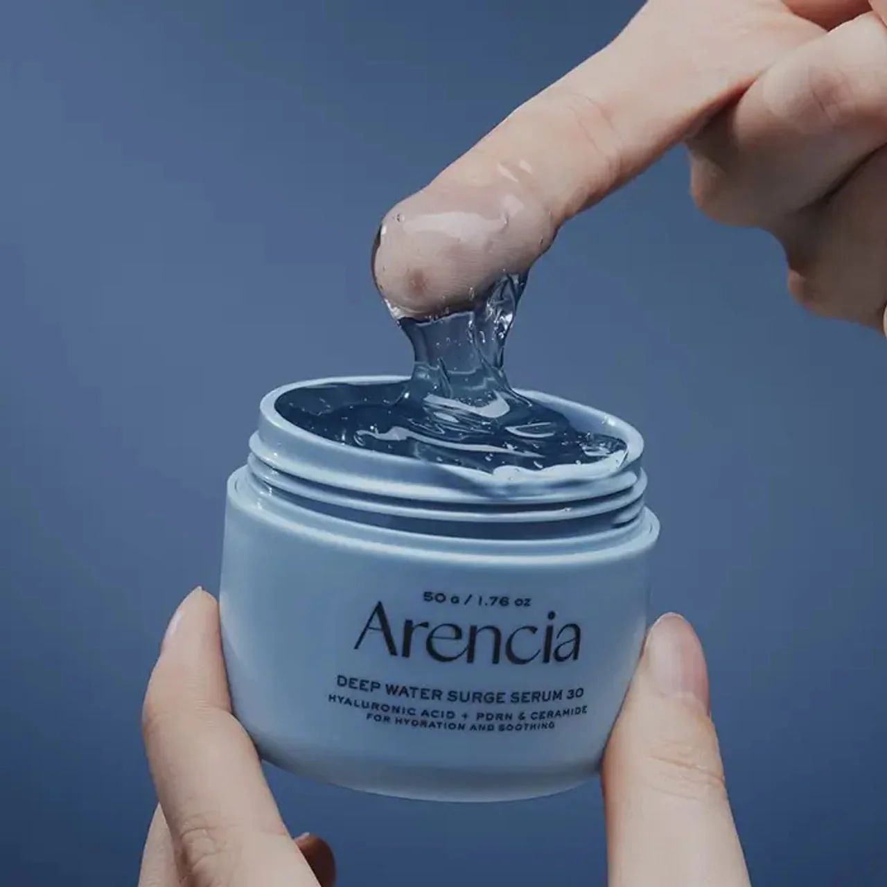 Hellblaue Dose mit AENCIA DEEP WATER SURGE SERUM 30. Klare Geltextur wird mit dem Finger entnommen.