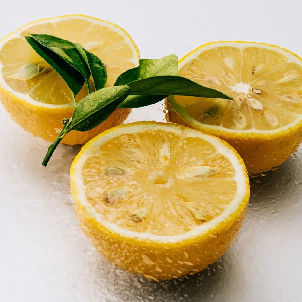 Drei halbierte Zitronen mit Blättern. Gelbe Frucht mit sichtbarem Fruchtfleisch. Auf einer glänzenden Oberfläche.