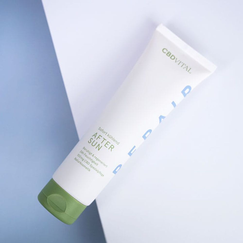 Weiße Tube mit grünem Deckel, diagonal auf weiß-blauem Hintergrund. Aufschrift: CBD VITAL, AFTER SUN, sofort kühlend, beruhigt & regeneriert, 24h Feuchtigkeit.