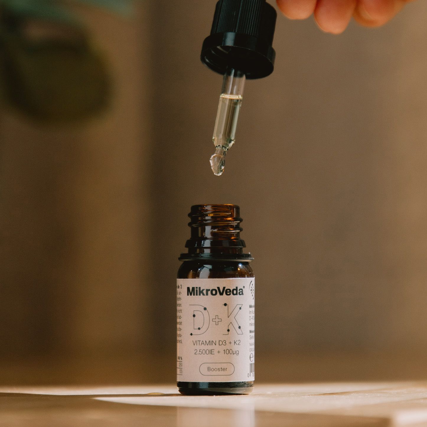 MikroVeda D+K Vitamin D3+K2 Booster Flasche mit Pipette, ein Tropfen fällt.