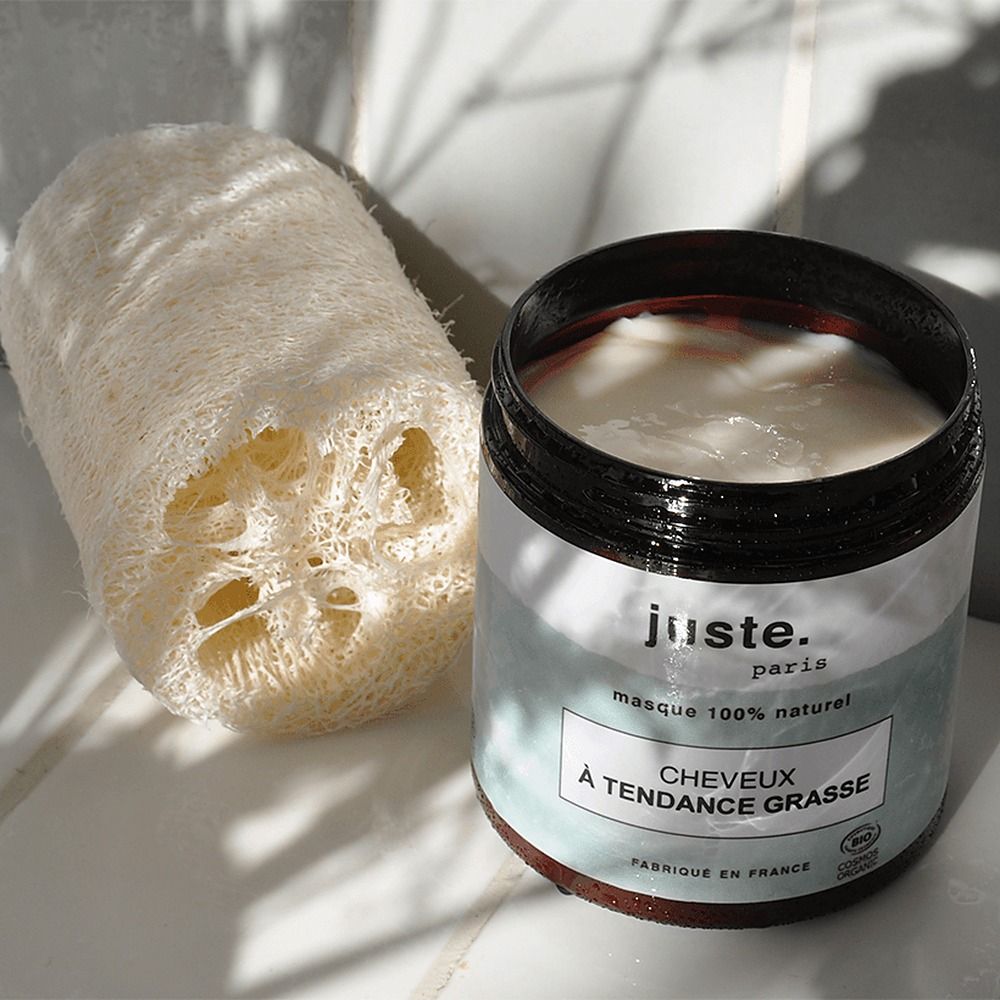 Ein Glasbehälter mit weißer Creme und ein Luffa-Schwamm liegen nebeneinander.