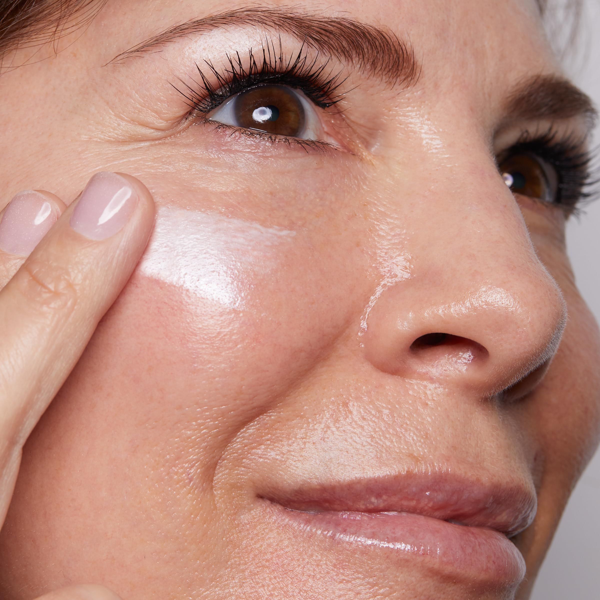 Eine Fingerspitze trägt CLARINS SOS Primer auf die Wange einer Frau auf.