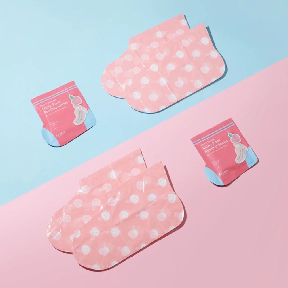 Zwei Paar rosa Fußmasken mit weißen Punkten und zwei Verpackungen. Text: Peach Vinegar Dirty Foot Peeling Socks. Marke FRUDIA.