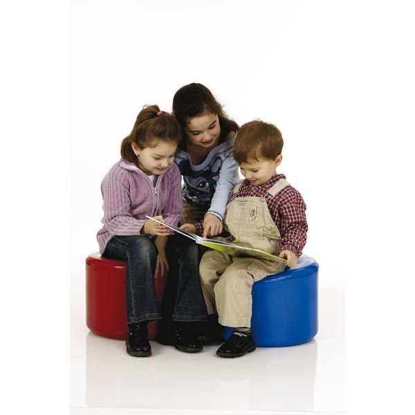 Drei Kinder sitzen auf roten und blauen Hockern und lesen gemeinsam ein Buch.
