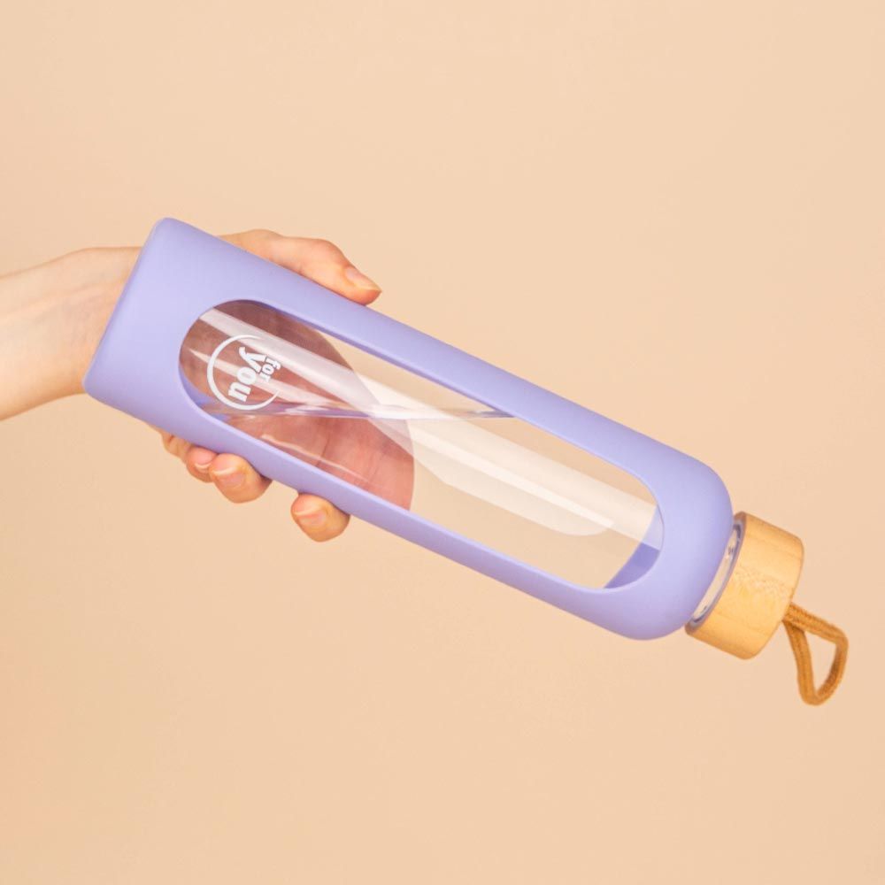 Glasflasche mit lila Silikonhülle und Bambusdeckel, gehalten in einer Hand.