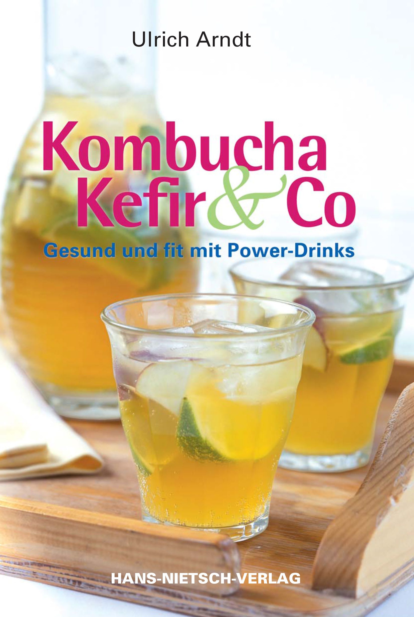 Buchcover: "Kombucha Kefir & Co" von Ulrich Arndt. Gläser mit Getränken, Limetten und Äpfeln auf Holztablett. Verlag: HANS-NIETSCH-VERLAG.