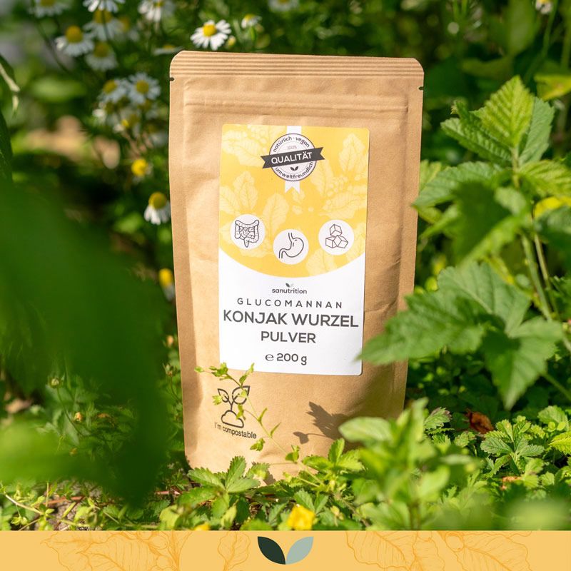 Braune Papiertüte mit Sanutrition Glucomannan Konjak Wurzel Pulver, umgeben von grünen Pflanzen. Aufdruck: 200g, Qualitätssiegel.