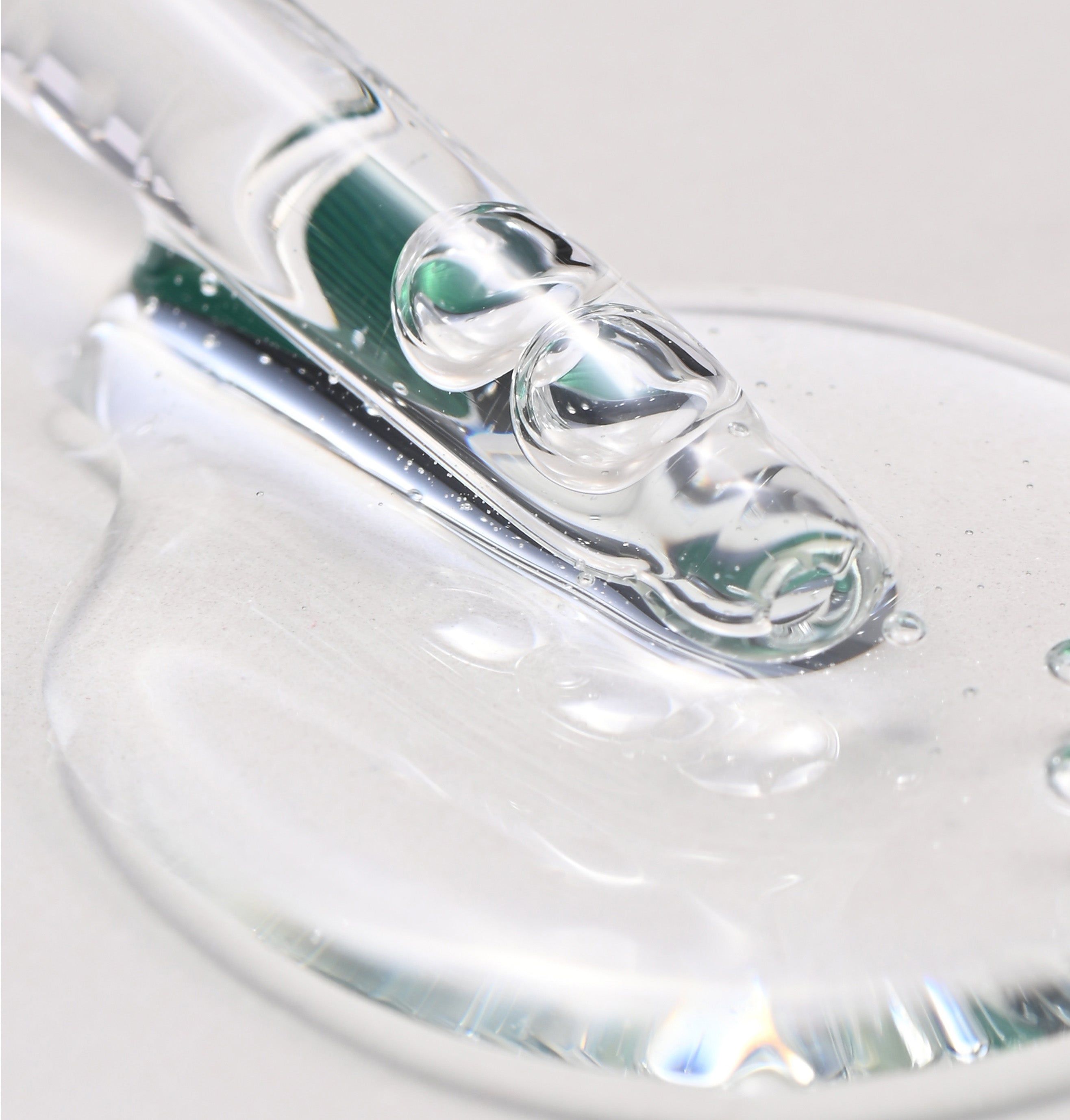 Nahaufnahme von transparentem Öl, das aus einer Pipette tropft. Leichte Reflexionen auf der Oberfläche.