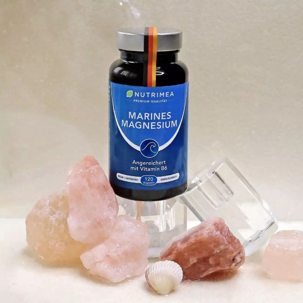 Flasche MAGNESIUM mit Vitamin B6, umgeben von rosa Steinen und einer Muschel. Mit deutschem Fähnchen.