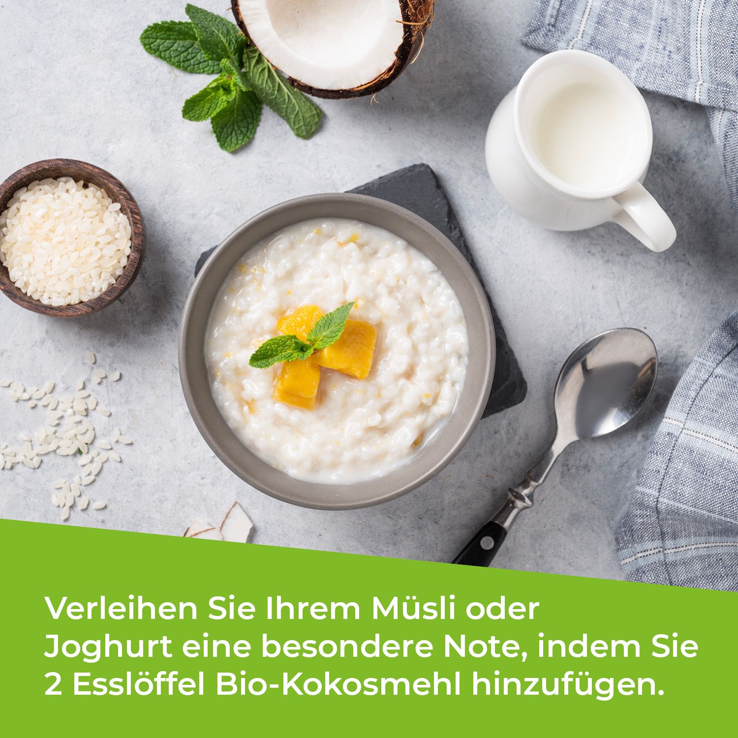 Schüssel mit Müsli, Joghurt, Mango-Stücken, Minze, Löffel, Milchkanne. Text: Verleihen Sie Ihrem Müsli oder Joghurt eine besondere Note, indem Sie 2 Esslöffel Bio-Kokosmehl hinzufügen.